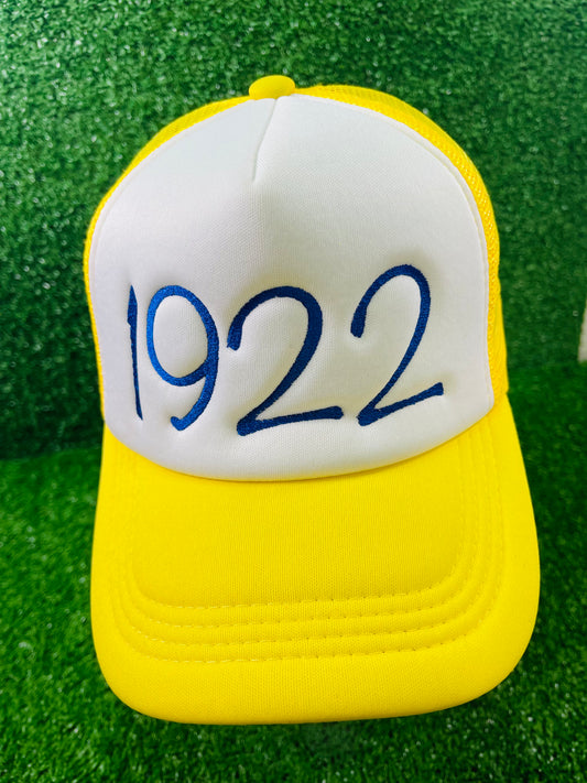 Front view of yellow and white trucker hat with 1922 embroidered in royal blue representing Sigma Gamma Rho Sorority Incorporated. 
Side view of hat showing a blue embroidered paw print on the yellow mesh panel.