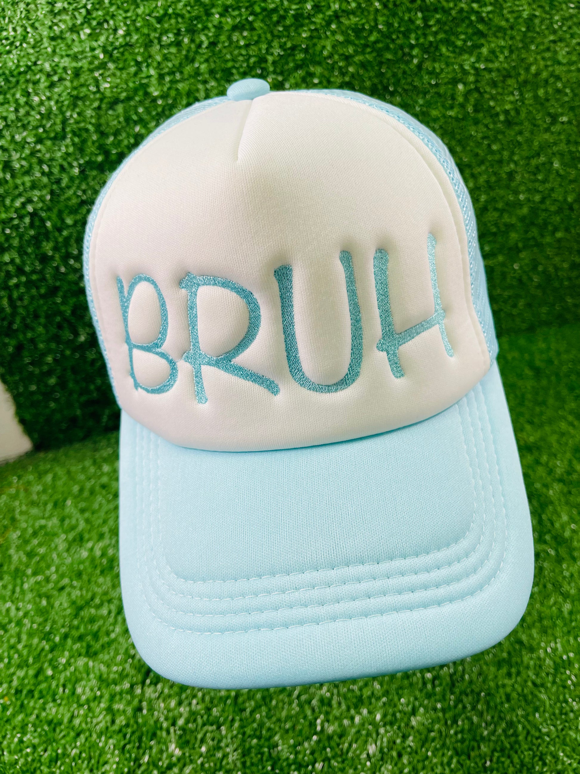 Embroidered BRUH trucker hat in baby blue and white, serving laid-back vibes with bold lettering, set against a grass-textured backdrop.