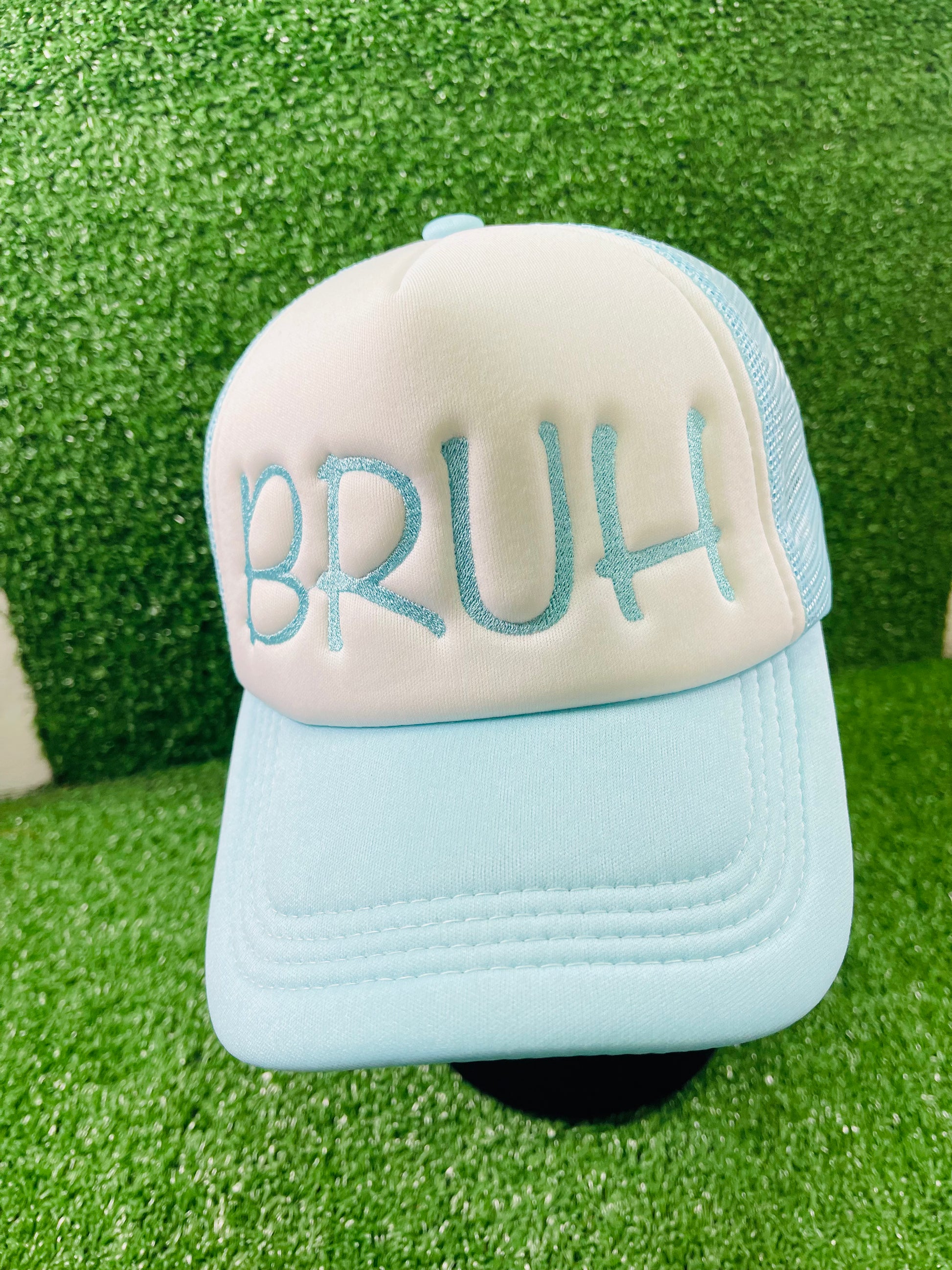 Light blue and white trucker hat with bold embroidery that reads BRUH on the front, displayed against a green turn background.