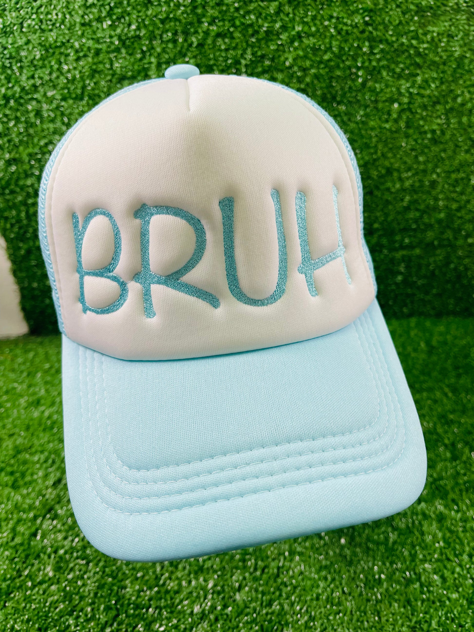Embroidered BRUH trucker hat in baby blue and white, serving laid-back vibes with bold lettering, set against a grass-textured backdrop.