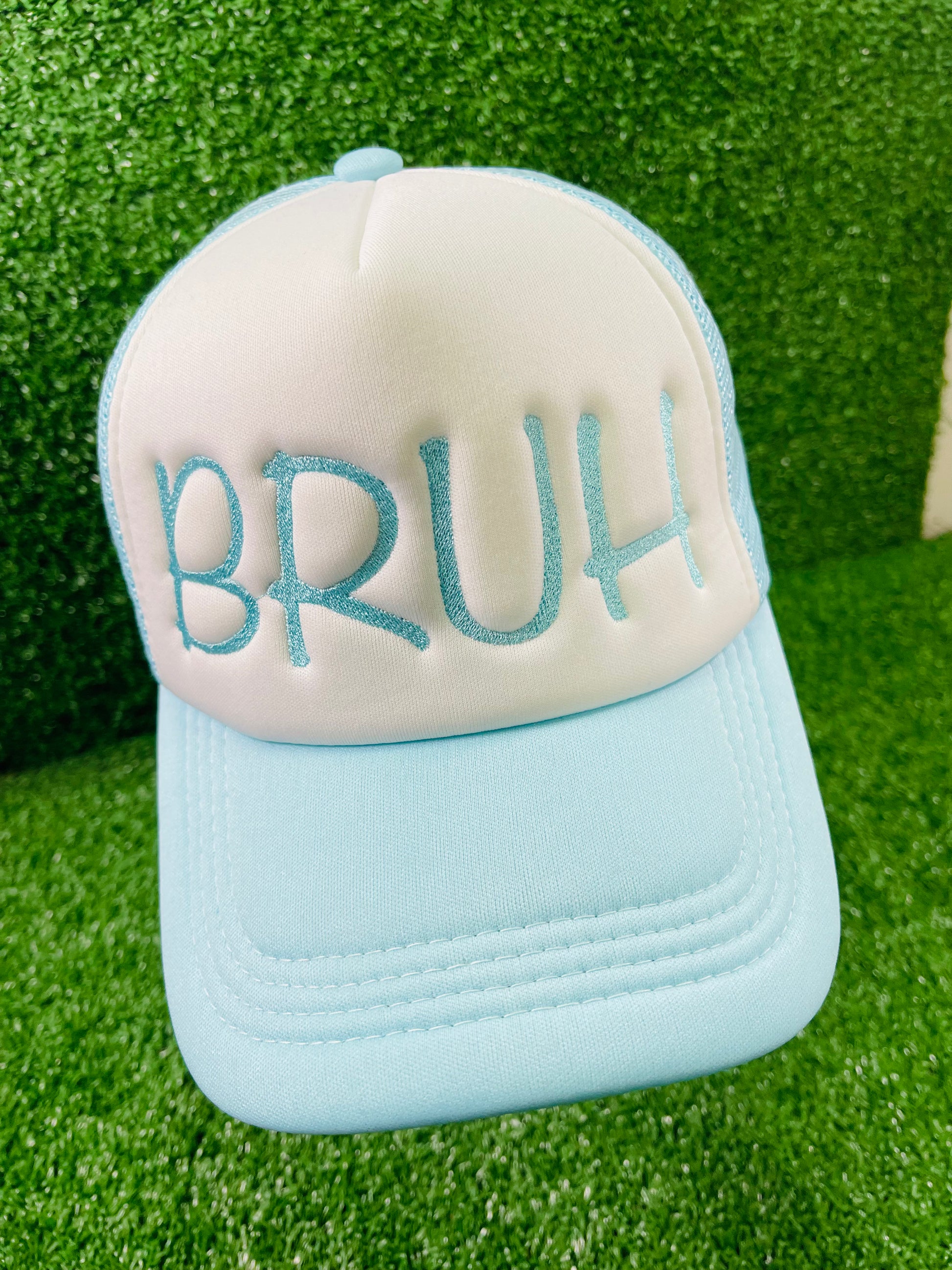 Embroidered BRUH trucker hat in baby blue and white, serving laid-back vibes with bold lettering, set against a grass-textured backdrop.
