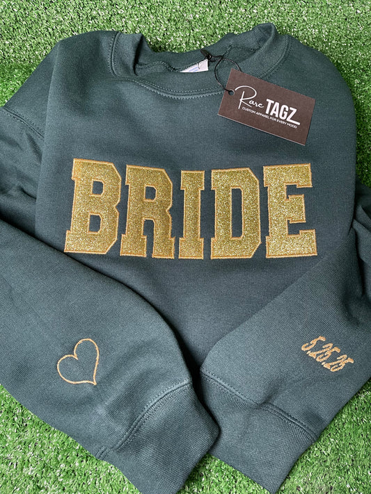 Custom BRIDE sweatshirt with gold glitter appliqué lettering featuring embroidered heart and wedding date details o the sleeves.