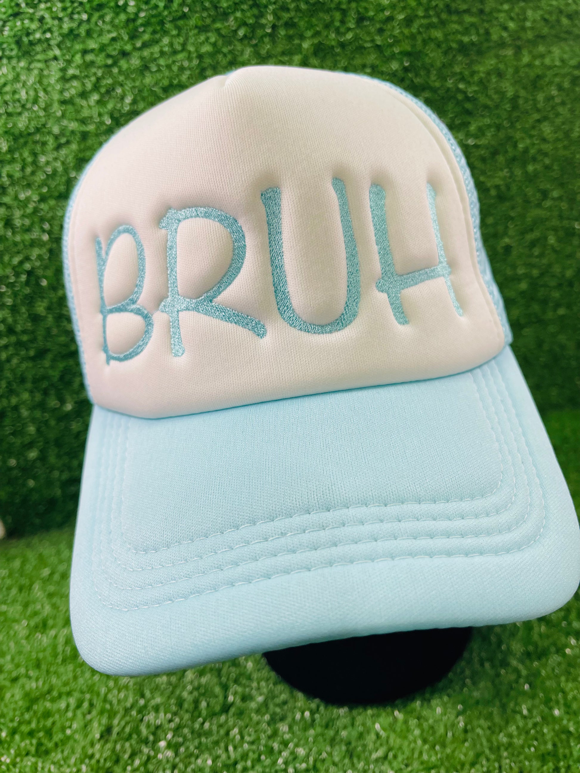 Embroidered BRUH trucker hat in baby blue and white, serving laid-back vibes with bold lettering, set against a grass-textured backdrop.