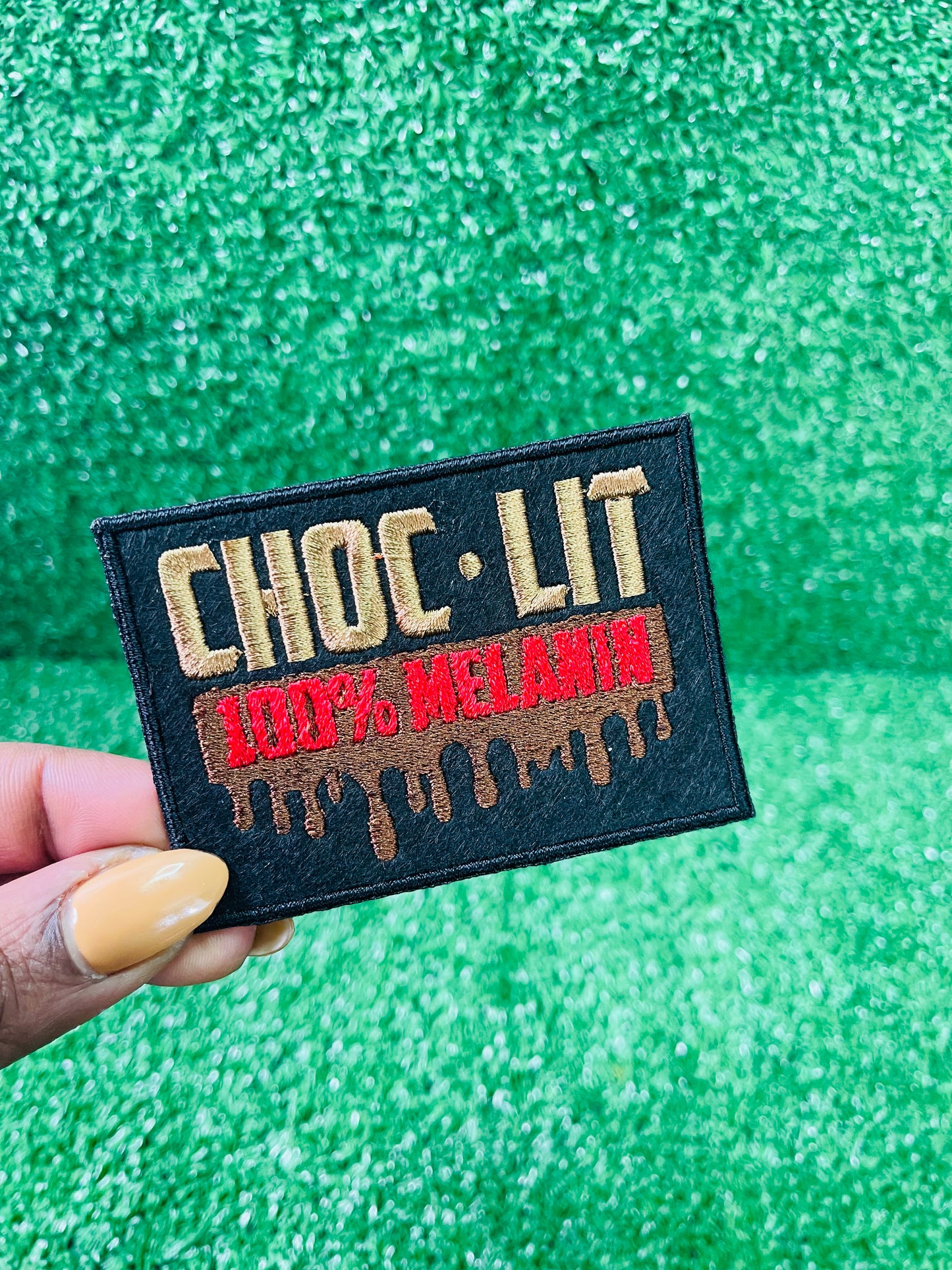 Embroidered patch reading Choc-Lit 100% Melanin with dripping chocolate effect, in bold black, red, and brown tones.