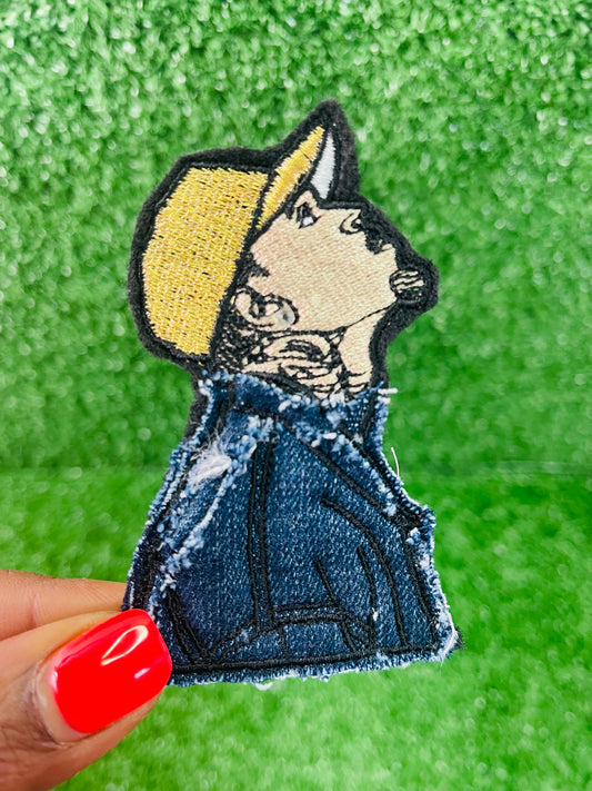 Embroidered patch of a person wearing a yellow hat and denim jacket held against a green background. Custom embroidered iron-on Chris Brown patch featuring detailed stitching and denim accents designed as a limited edition tour inspired collectible.
