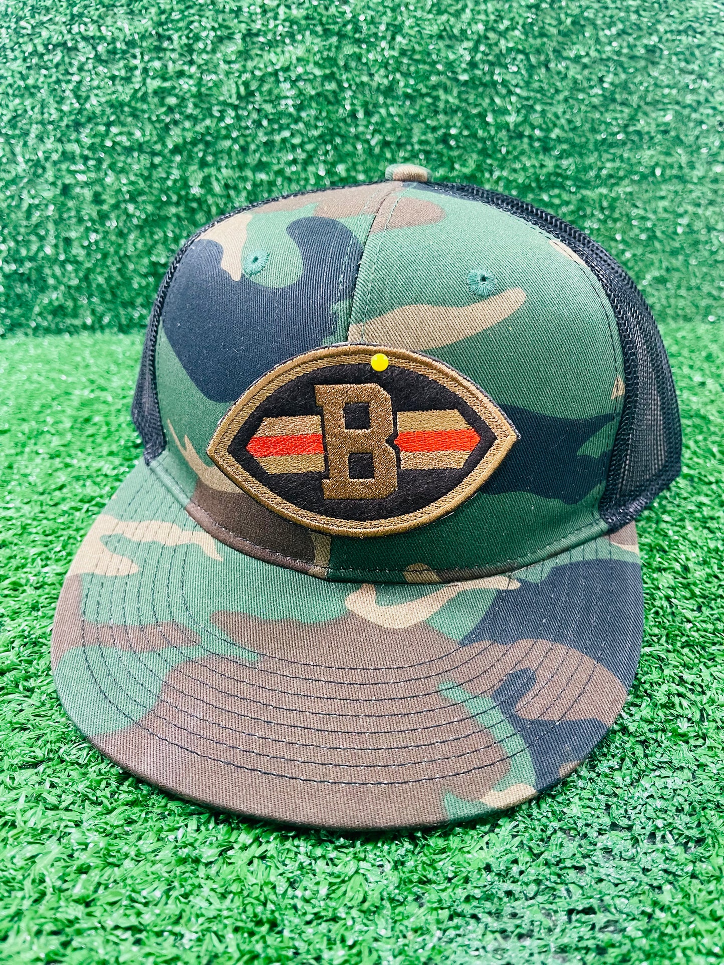 Close-up of embroidered patch shaped like a football with a Brown B in the center, dark brown background, and orange/gold stripes across each side.