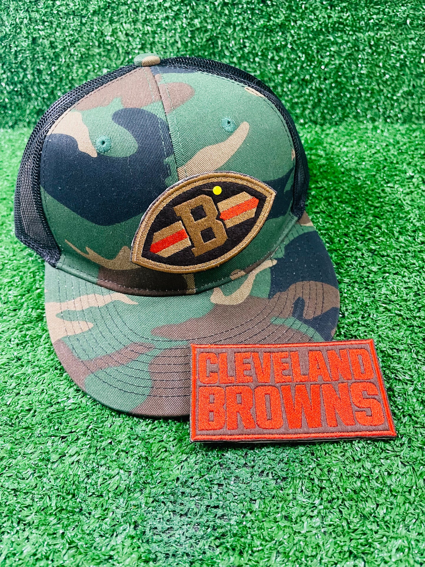 Close-up of embroidered patch shaped like a football with a Brown B in the center, dark brown background, and orange/gold stripes across each side.