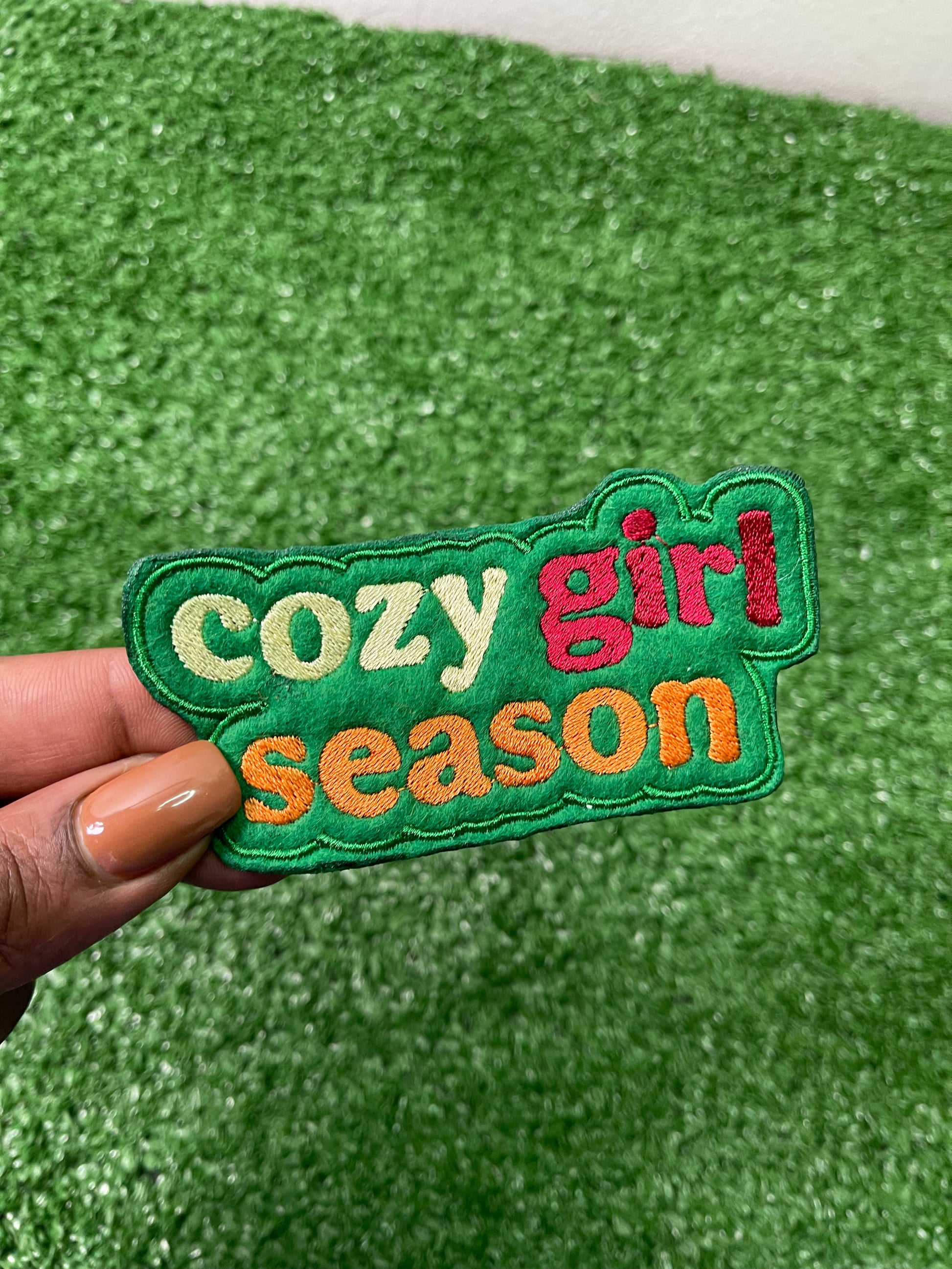 Colorful embroidered Cozy Girl Season iron-on patch with bold retro lettering in cream, burnt orange, green and red.