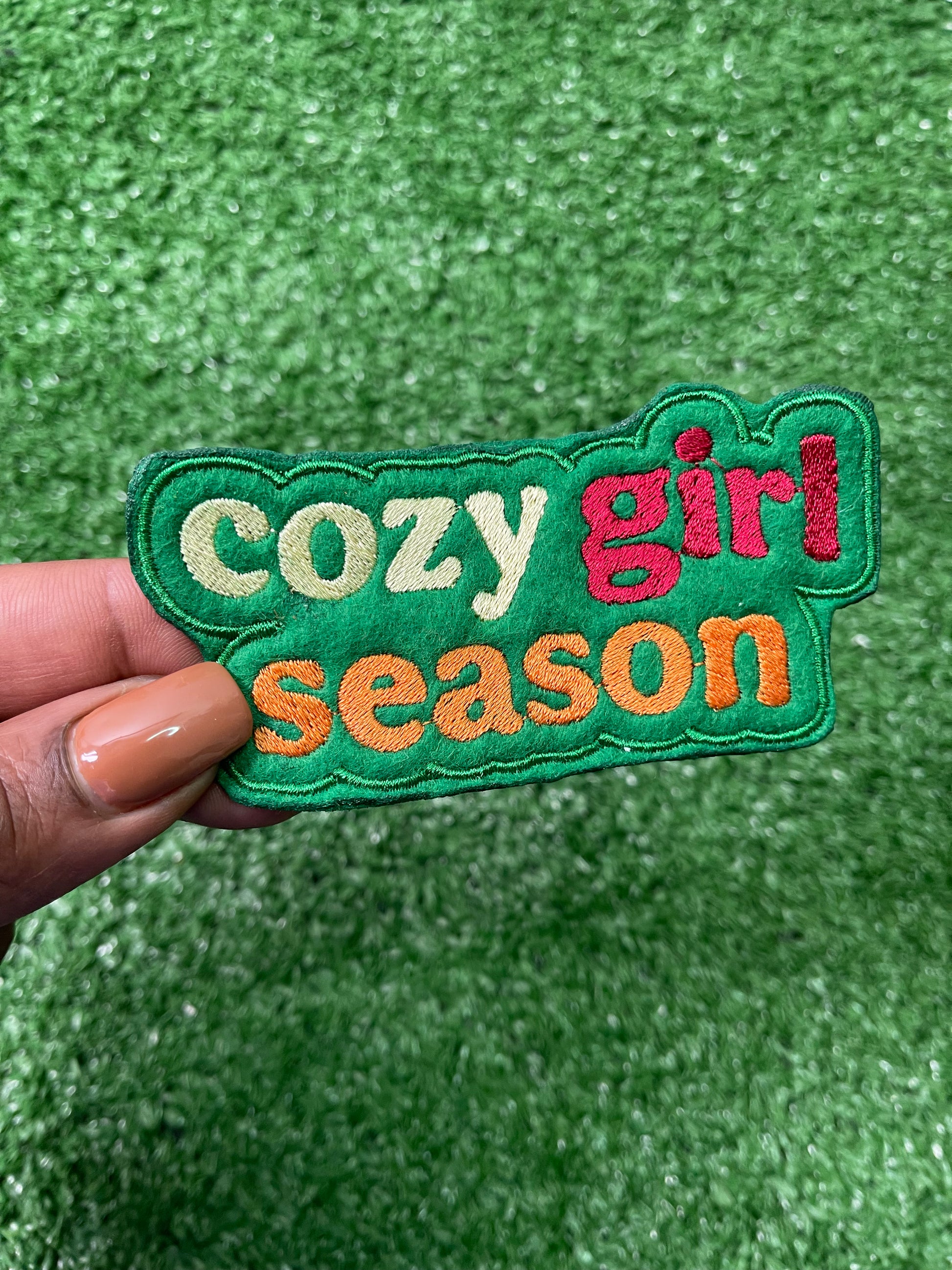 Colorful embroidered Cozy Girl Season iron-on patch with bold retro lettering in cream, burnt orange, green and red.