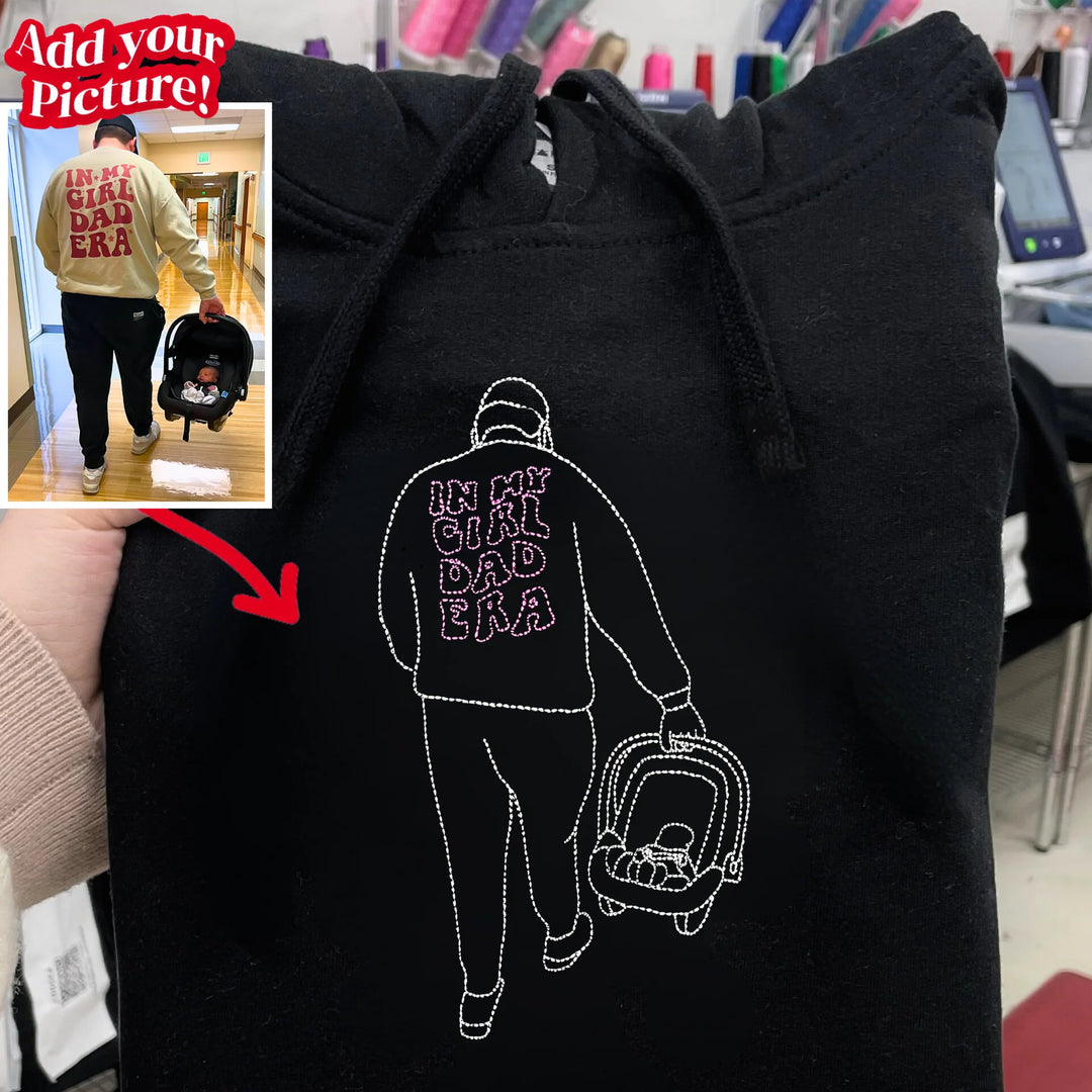 Custom embroidered hoodie featuring a line art outline of a father carrying a baby car seat with IN MY GIRL DAD ERA stitched on the back.