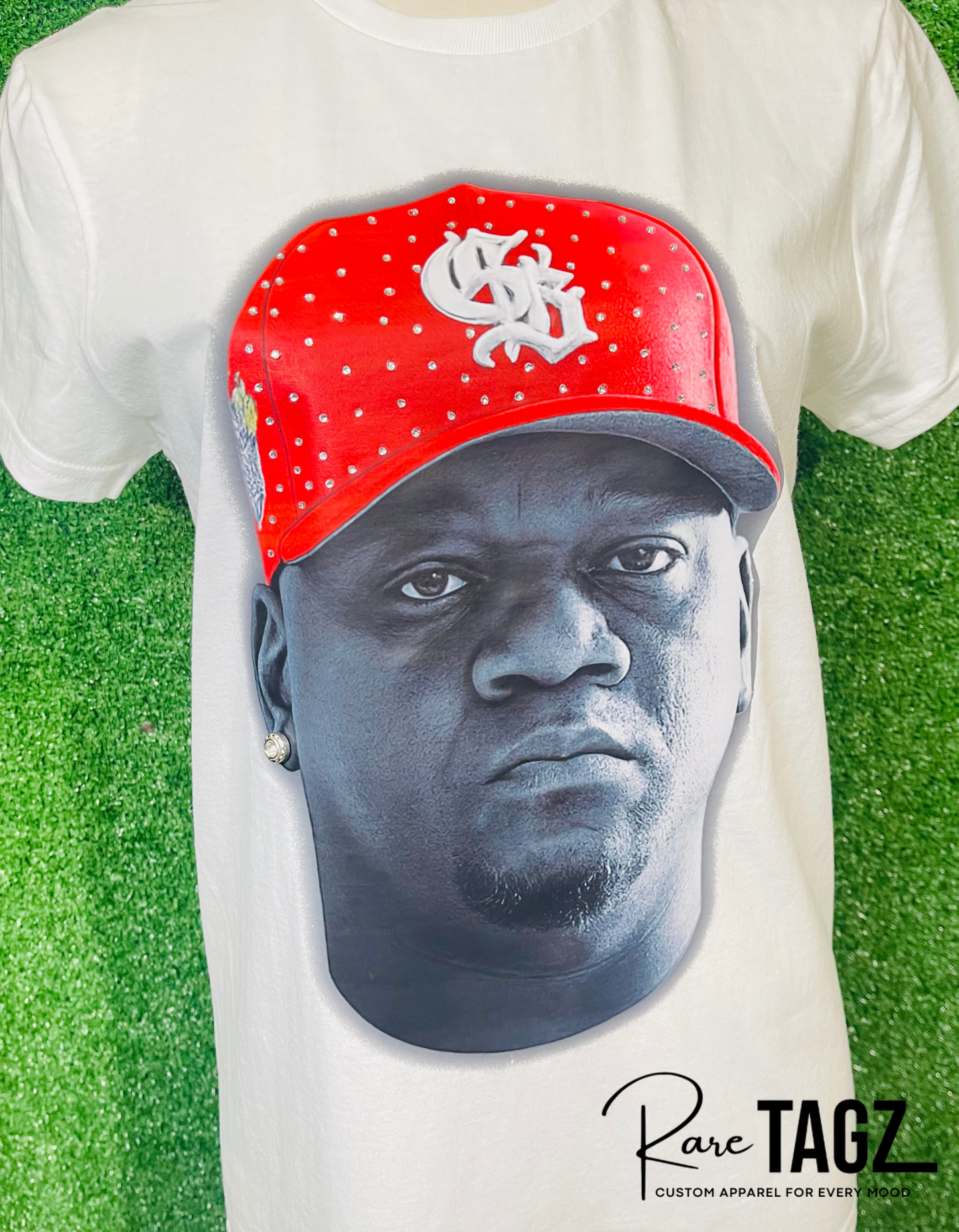 White t-shirt with a graphic of a face wearing a red cap on a grass background, featuring the brand 'Rare TAGZ'.
Custom DJ Fresh portrait t-shirt with hand placed rhinestones on red cap. Custom Breezy Tour shirt by Rare Tagz.