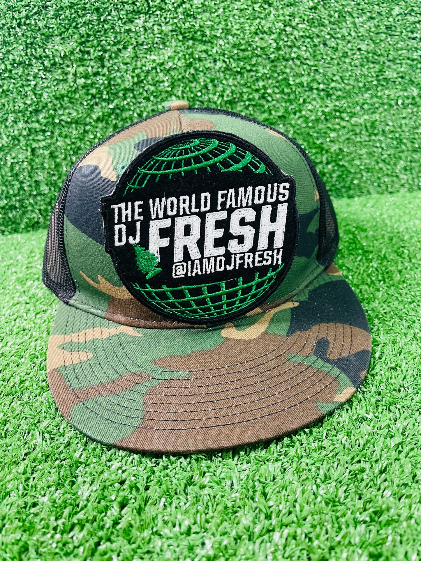 Camouflage cap with 'The World Famous DJ Fresh' logo on a green grass background