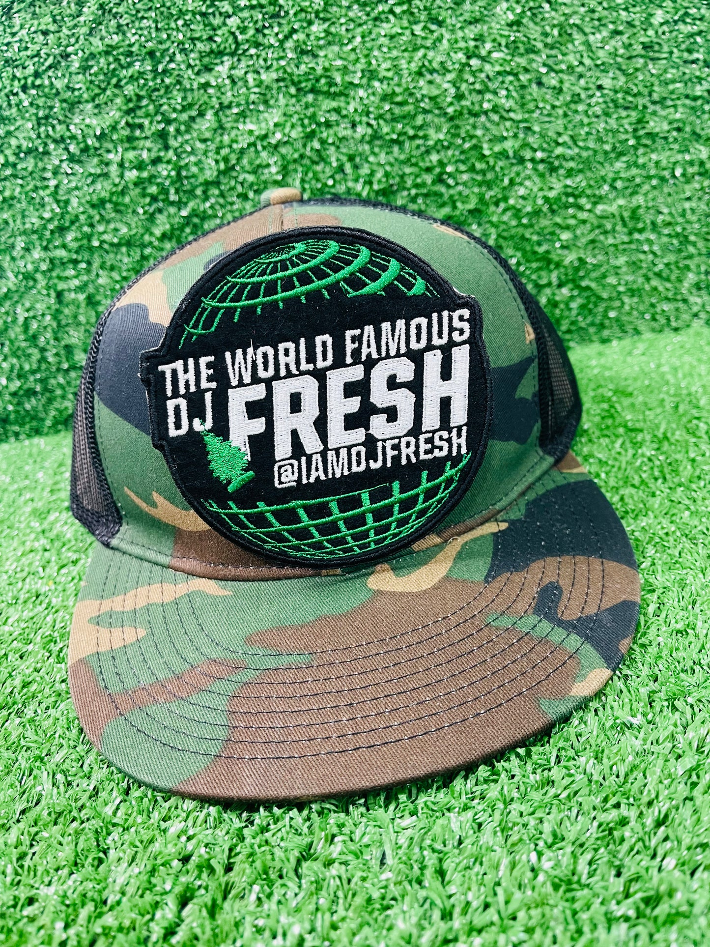 Camouflage cap with 'The World Famous DJ Fresh' logo on a green grass background