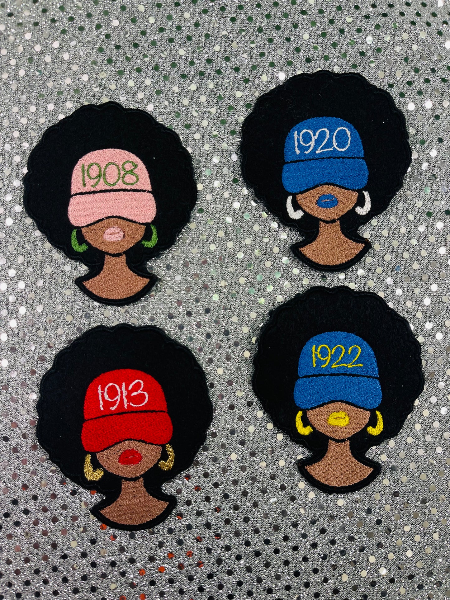 Four embroidered patches of women with styled hair and vintage hats on a textured background. The women are wearing different caps with the year their sorority was founded.