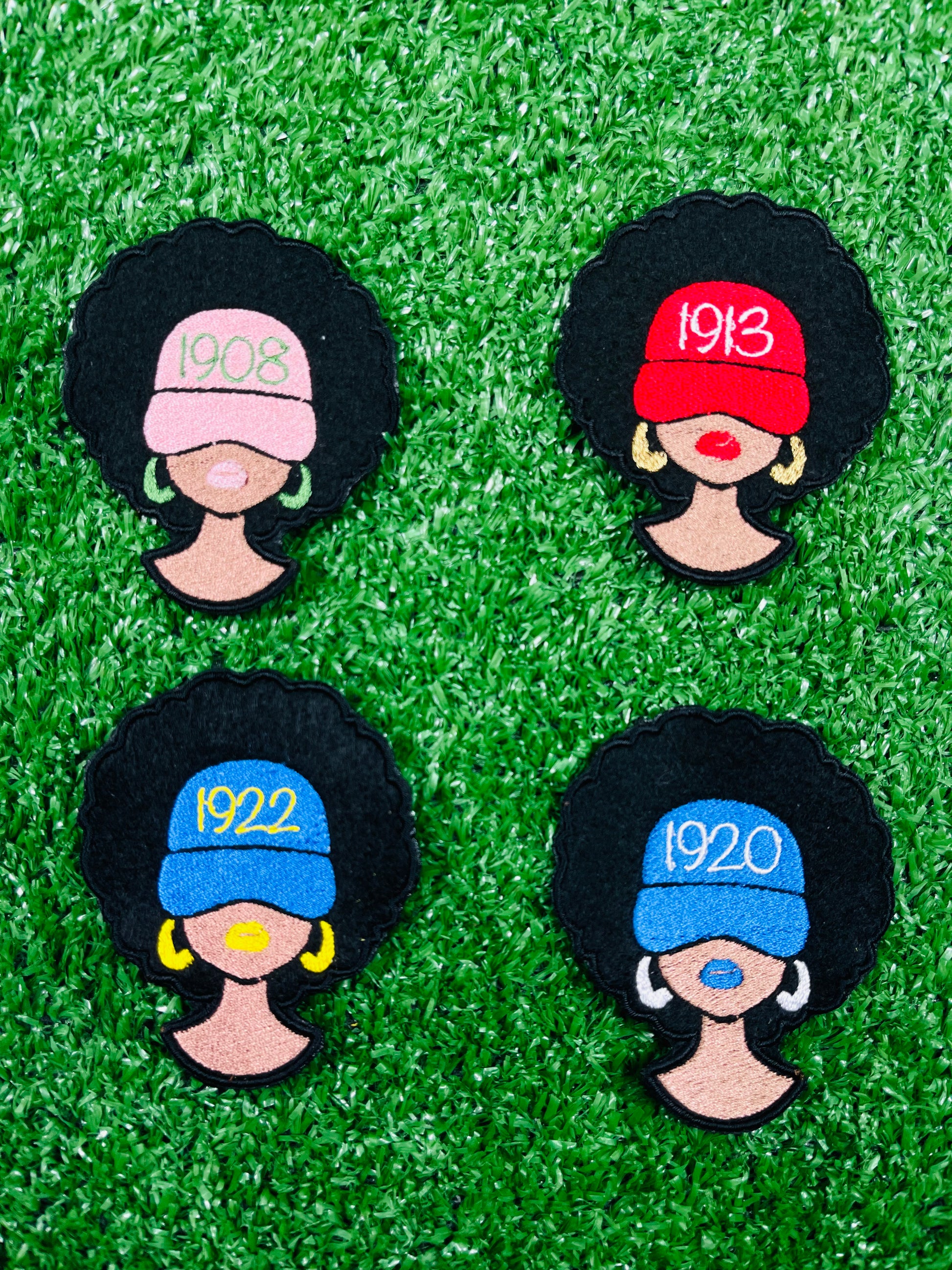Four decorative pins with black hair, colorful hats, and numbers on a green grass-like background.