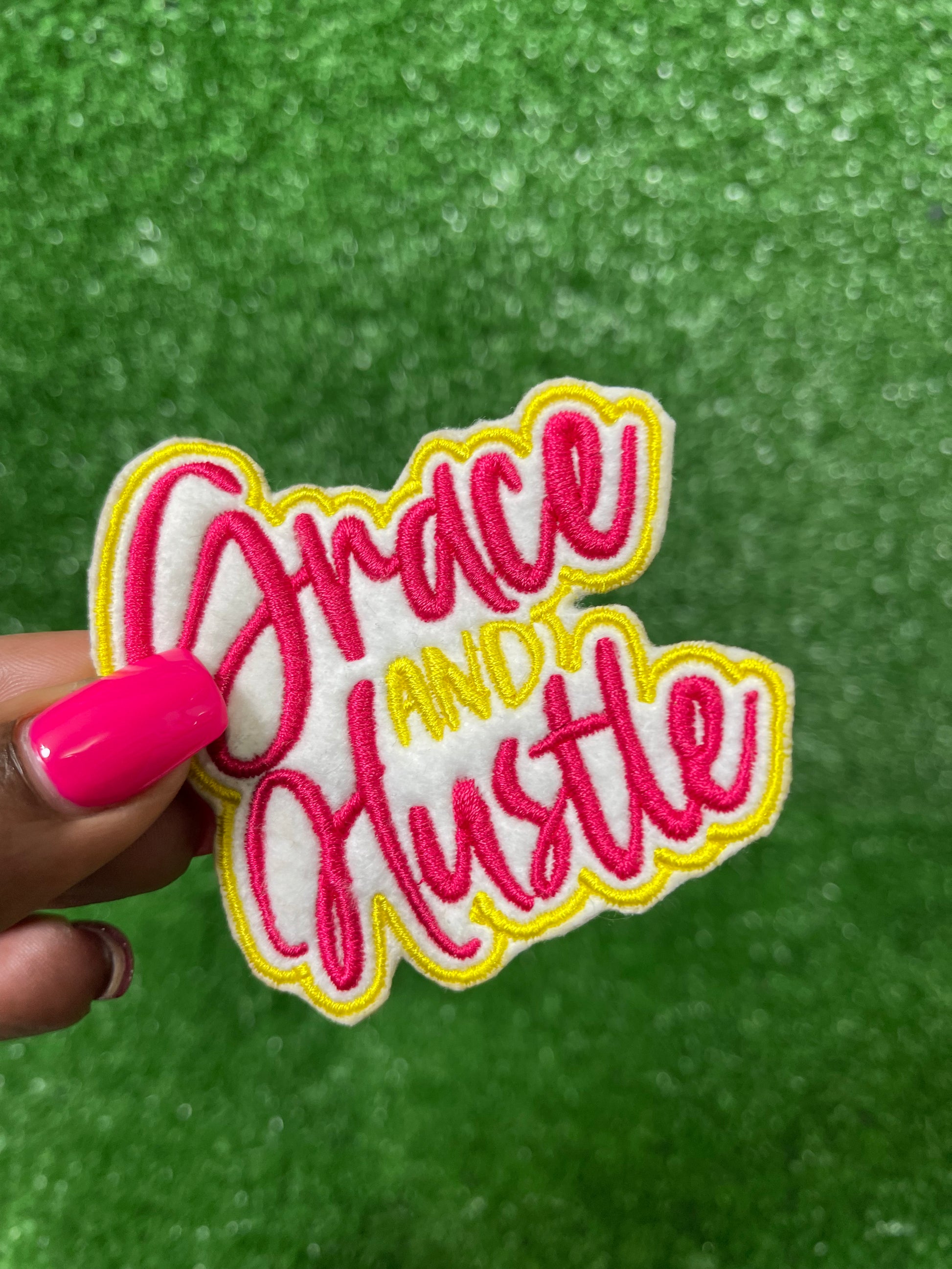 Grace and Hustle embroidered iron-on patch in bold pink and yellow thread with white background. Motivational iron-on patch for jackets, bags, and custom appearel.