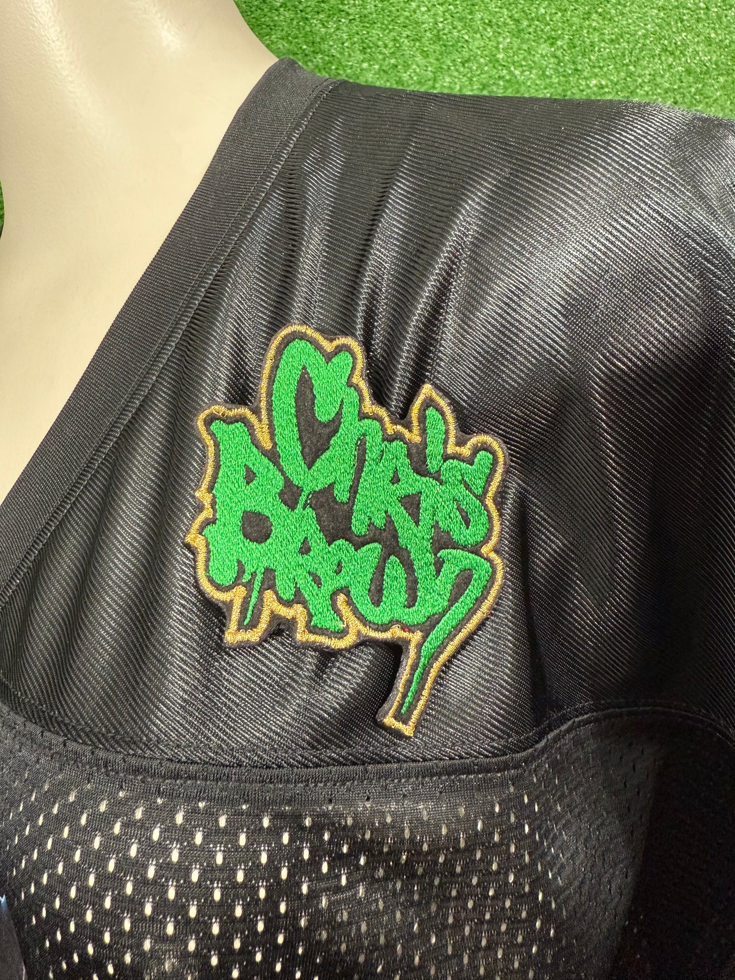 Black jacket with a green and yellow logo patch on a green backgroundBlack sports jersey with gold logo on a mannequin against a green background. Custom-made Chris Brown-inspired embroidered patches held against a vibrant green background. One patch features black graffiti-style text with a white base and gold outline; the other features red text with a white base and black outline. Designed and stitched in-house.
