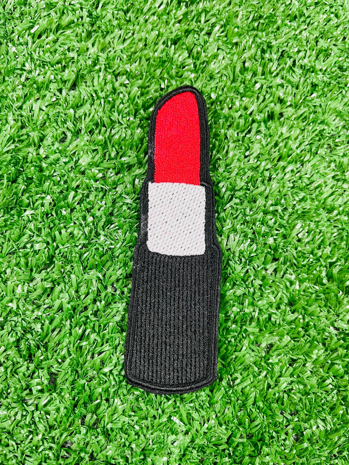 Lipstick-shaped object with red top and gray bottom on a green grass background