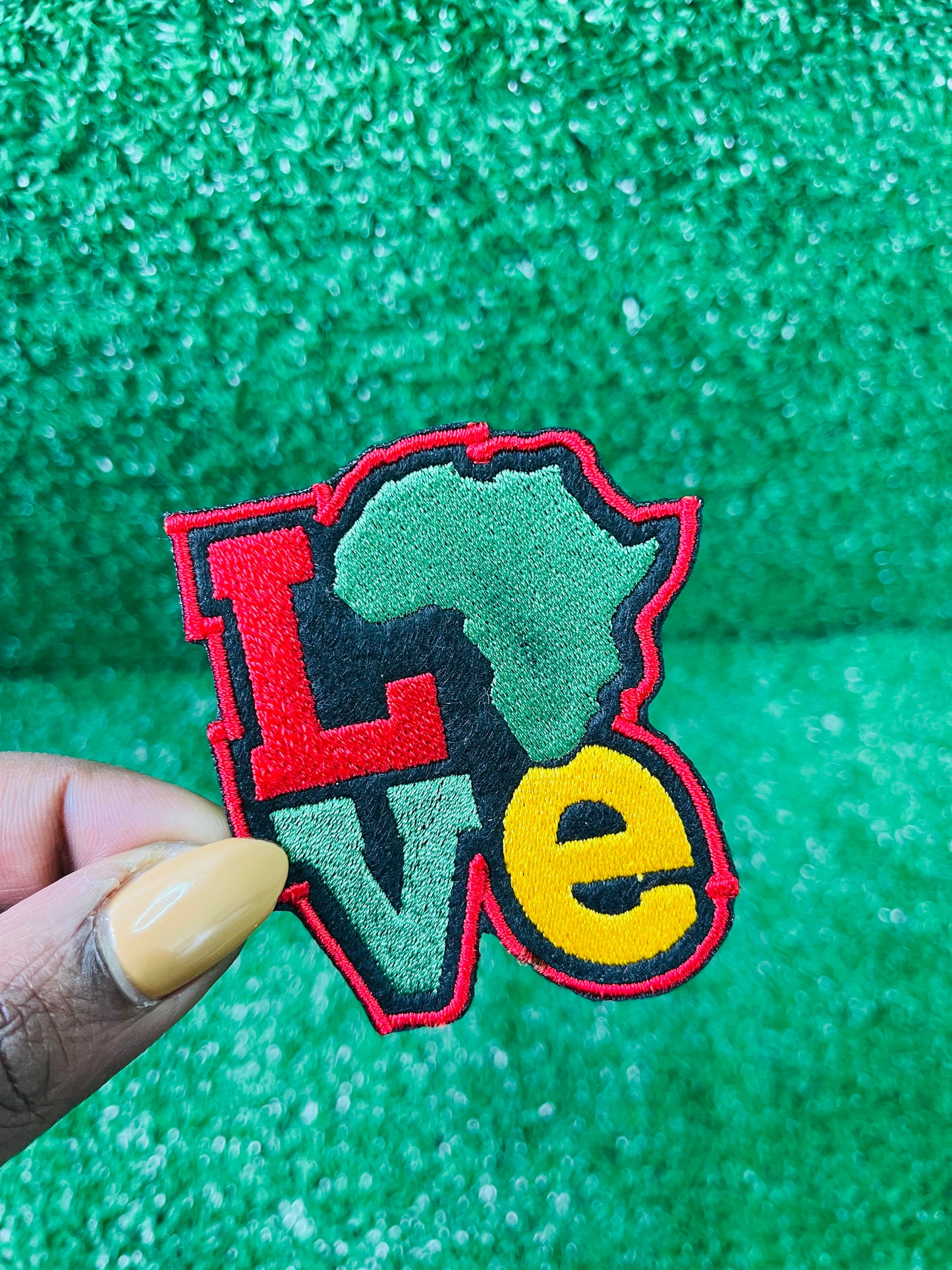 Colorful embroidered iron on patch spelling LOVE with the African continent as the "O" in red, yellow, green and black tones, bold and vibrant design.