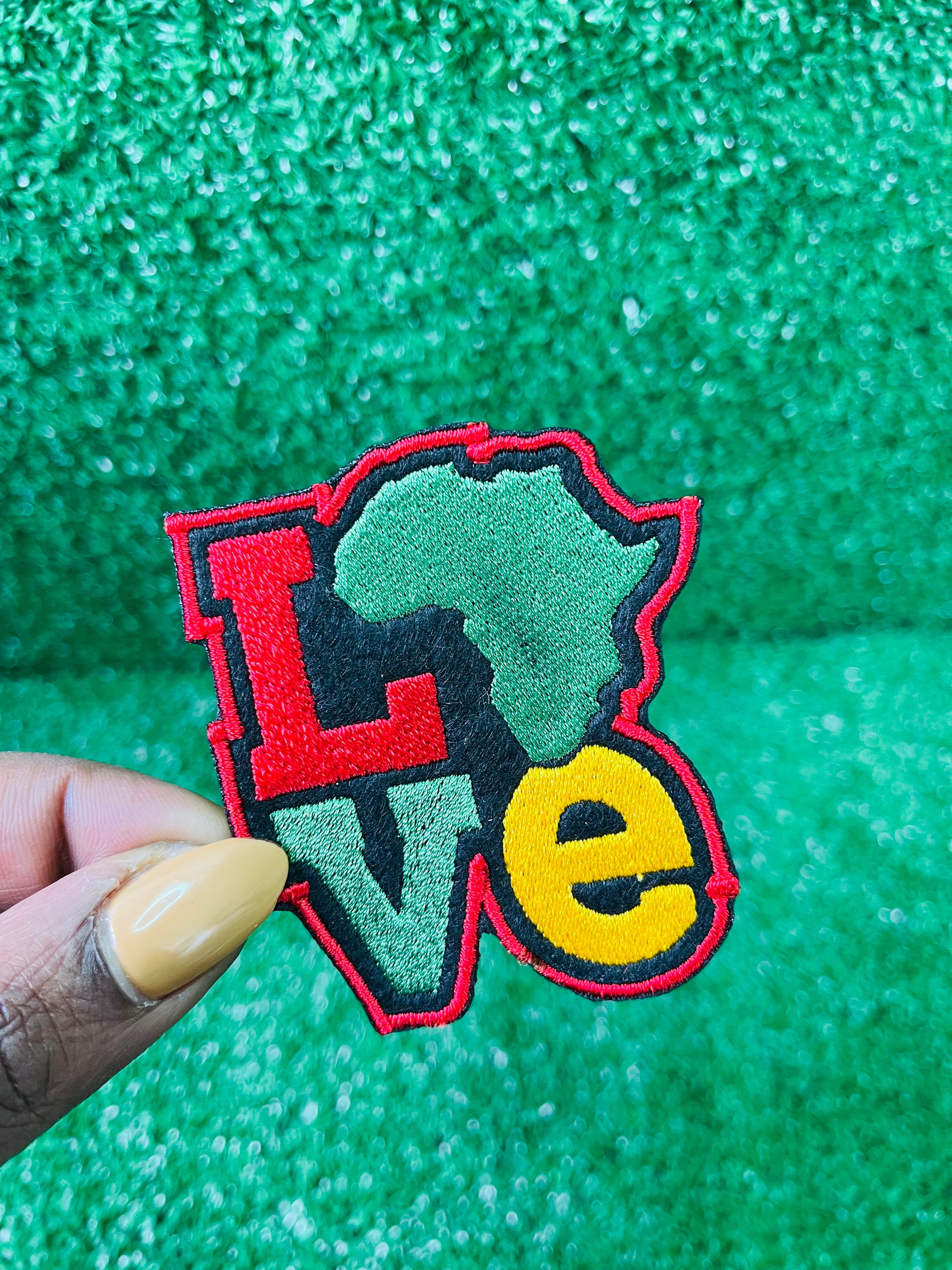 Colorful embroidered iron on patch spelling LOVE with the African continent as the "O" in red, yellow, green and black tones, bold and vibrant design.