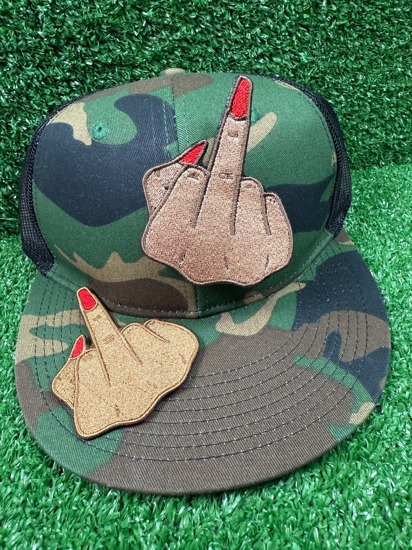 Camouflage cap with middle finger patches on a green grass background