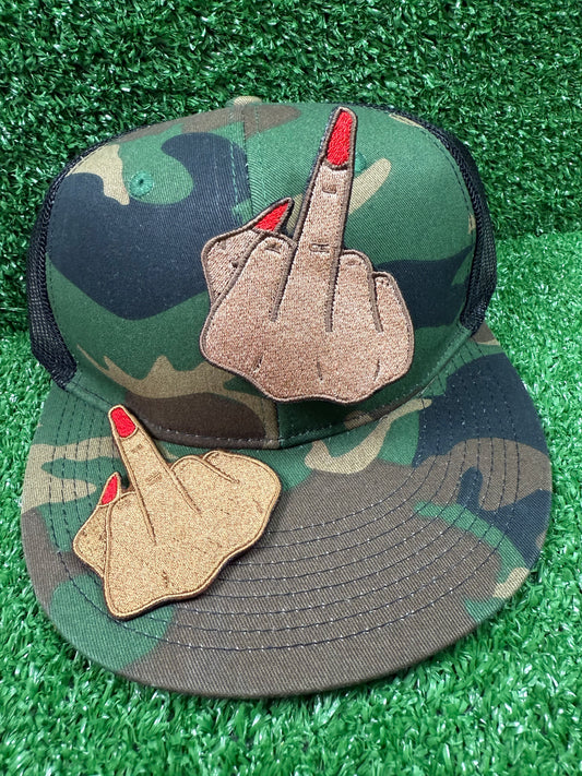 Camouflage cap with middle finger patches on a green grass background
