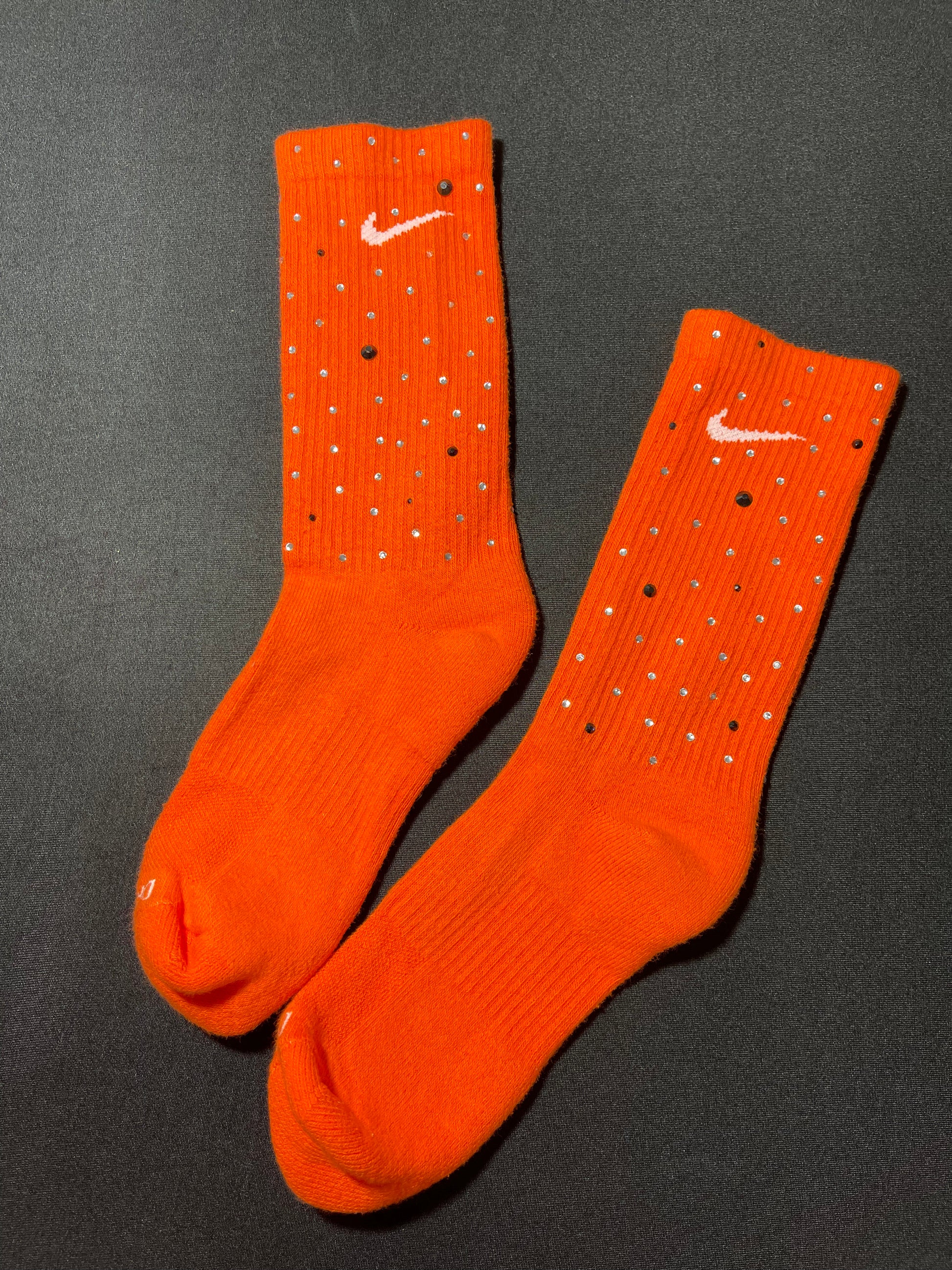 Orange Nike socks embellished with sparkling rhinestones, adding a touch of bling and style.  The socks feature a bold orange color with rhinestones carefully placed for a dazzling effect, perfect for elevating any sneaker look.