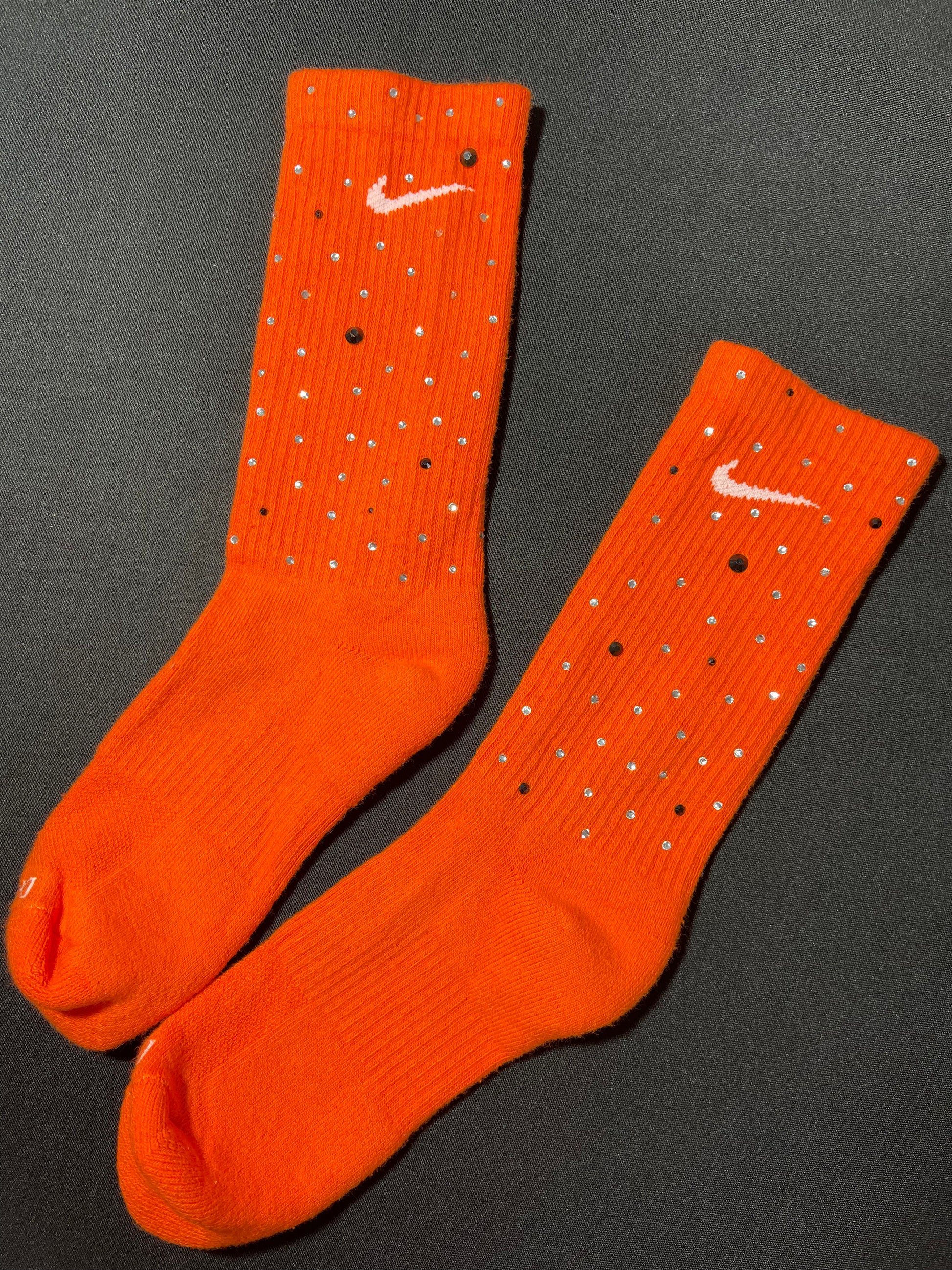 Orange Nike socks embellished with sparkling rhinestones, adding a touch of bling and style.  The socks feature a bold orange color with rhinestones carefully placed for a dazzling effect, perfect for elevating any sneaker look.