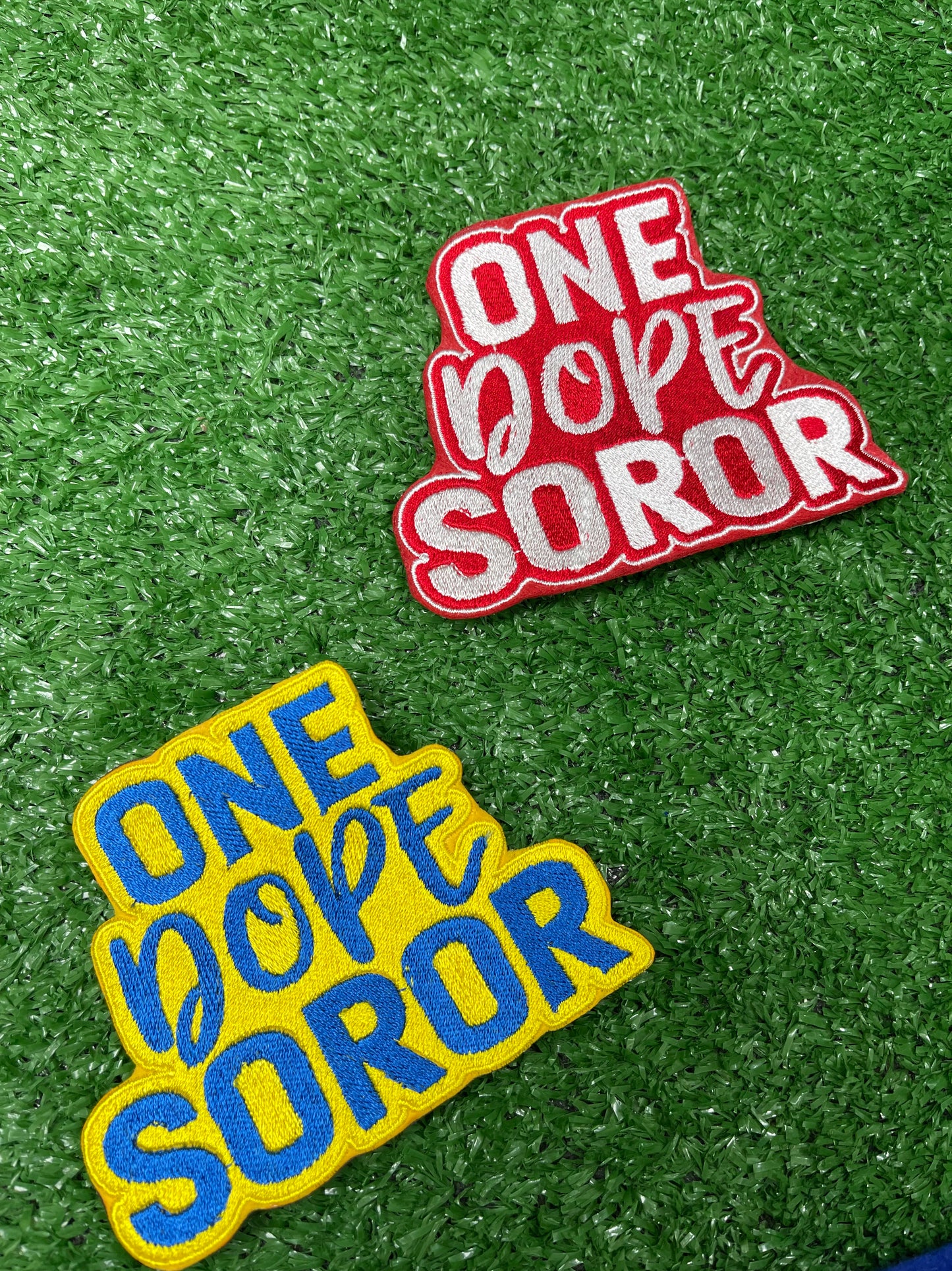 Embroidered patch with bold red and white lettering that says One Dope Soror on a green grass background. Also a patch in yellow and gold