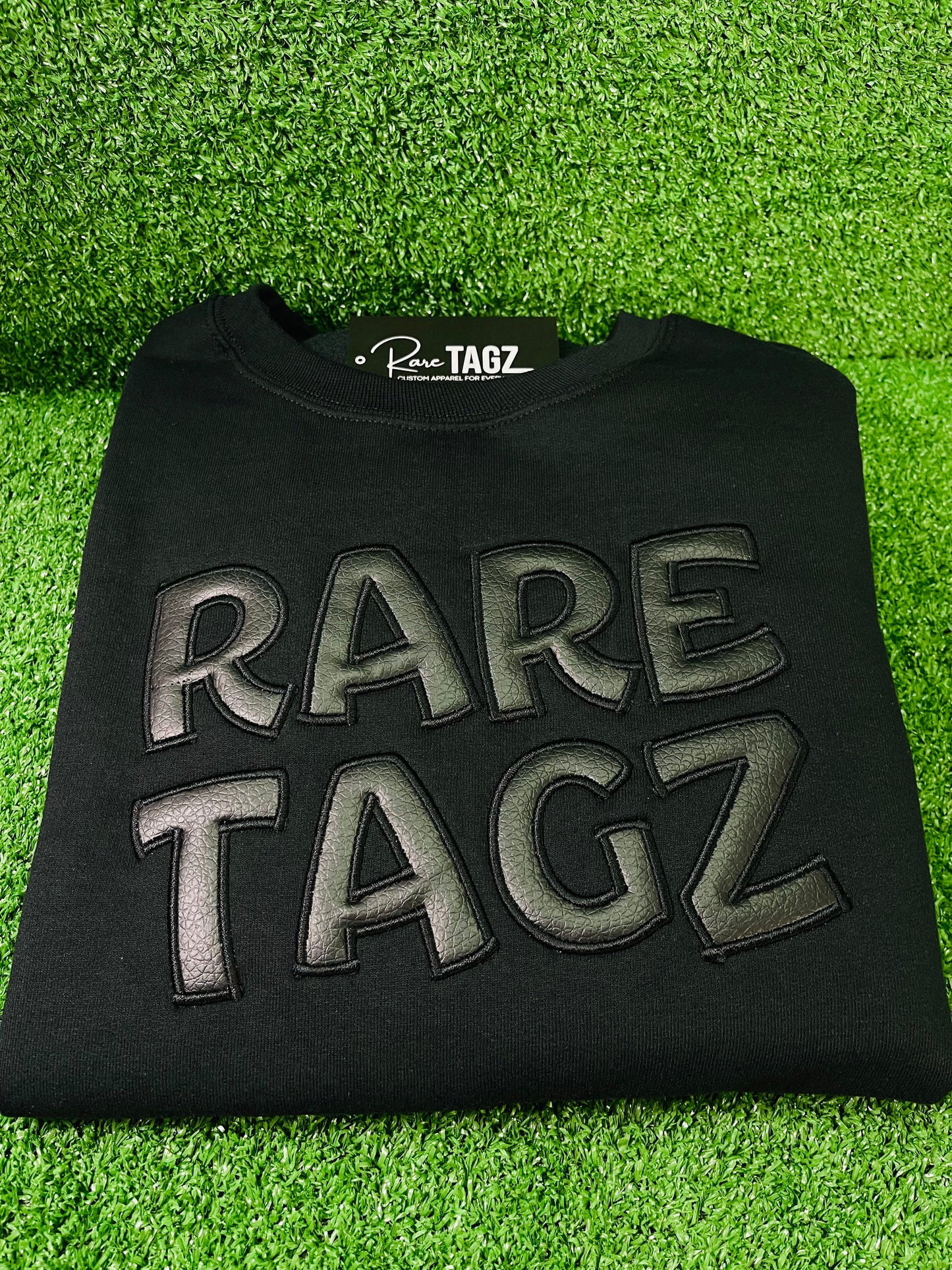 Black Sweatshirt featuring bold raised faux leather Rare Tagz lettering showcasing sleek design and premium craftsmanship.