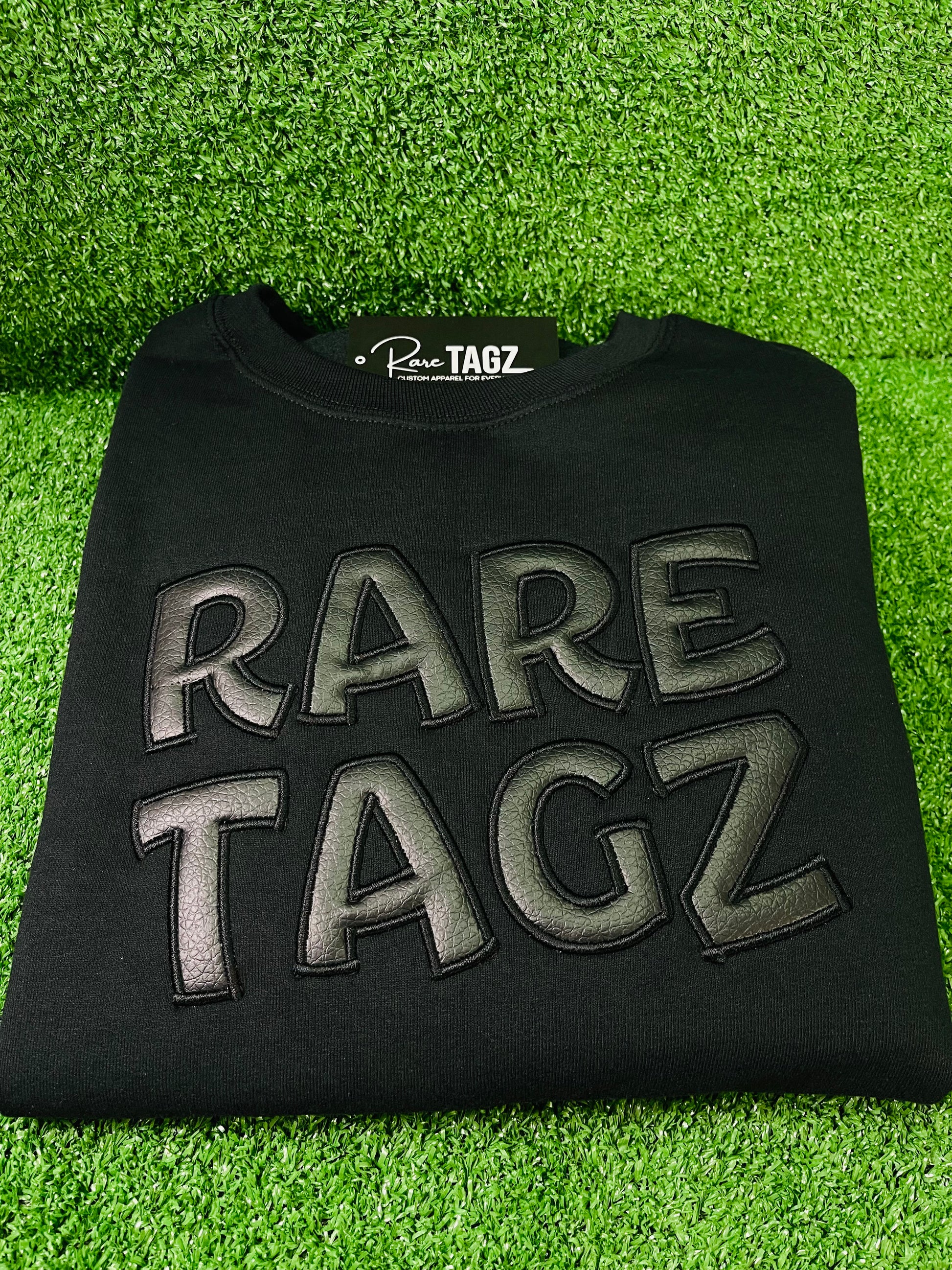 Black Sweatshirt featuring bold raised faux leather Rare Tagz lettering showcasing sleek design and premium craftsmanship.