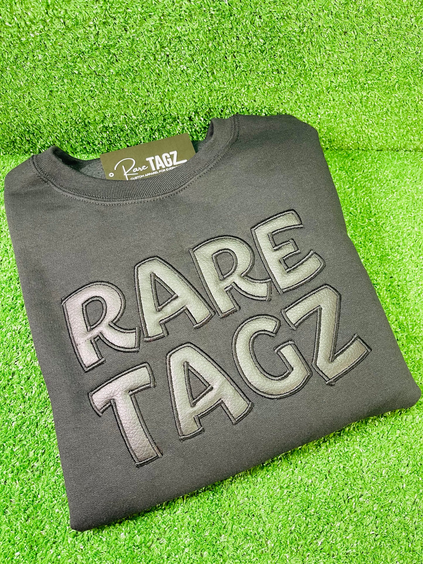 Black Sweatshirt featuring bold raised faux leather Rare Tagz lettering showcasing sleek design and premium craftsmanship.