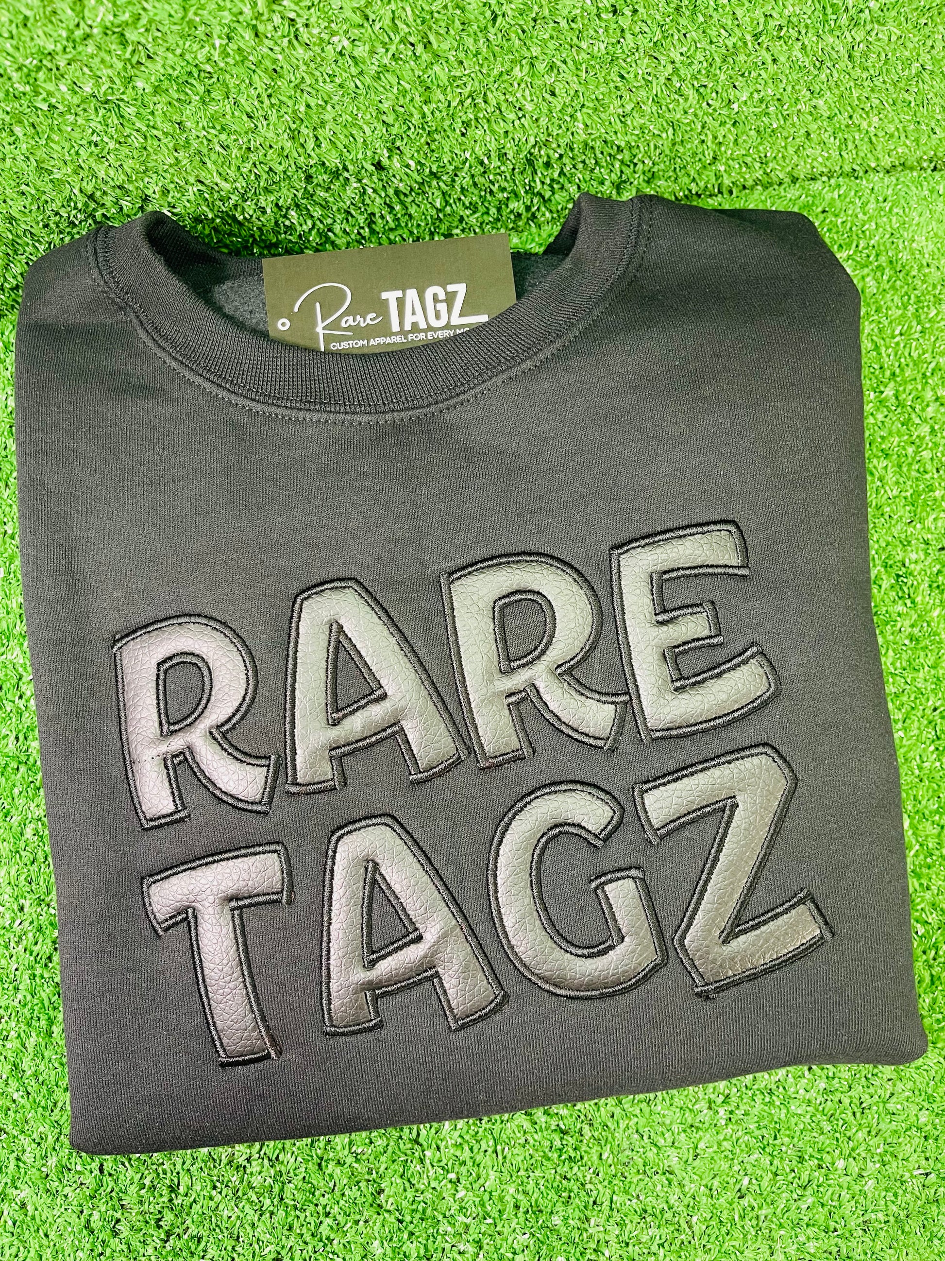 Black Sweatshirt featuring bold raised faux leather Rare Tagz lettering showcasing sleek design and premium craftsmanship.