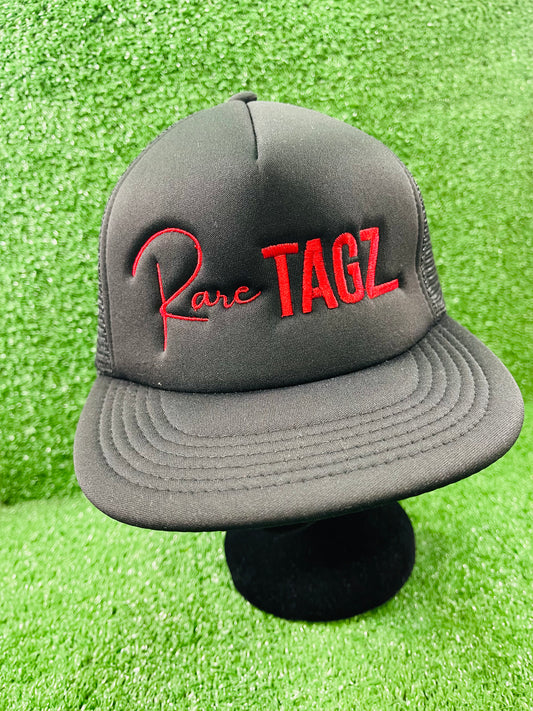 Front view of black trucker hat with red "Rare Tagz" embroidery. Side angle of hat showing clean stitching and mesh back.