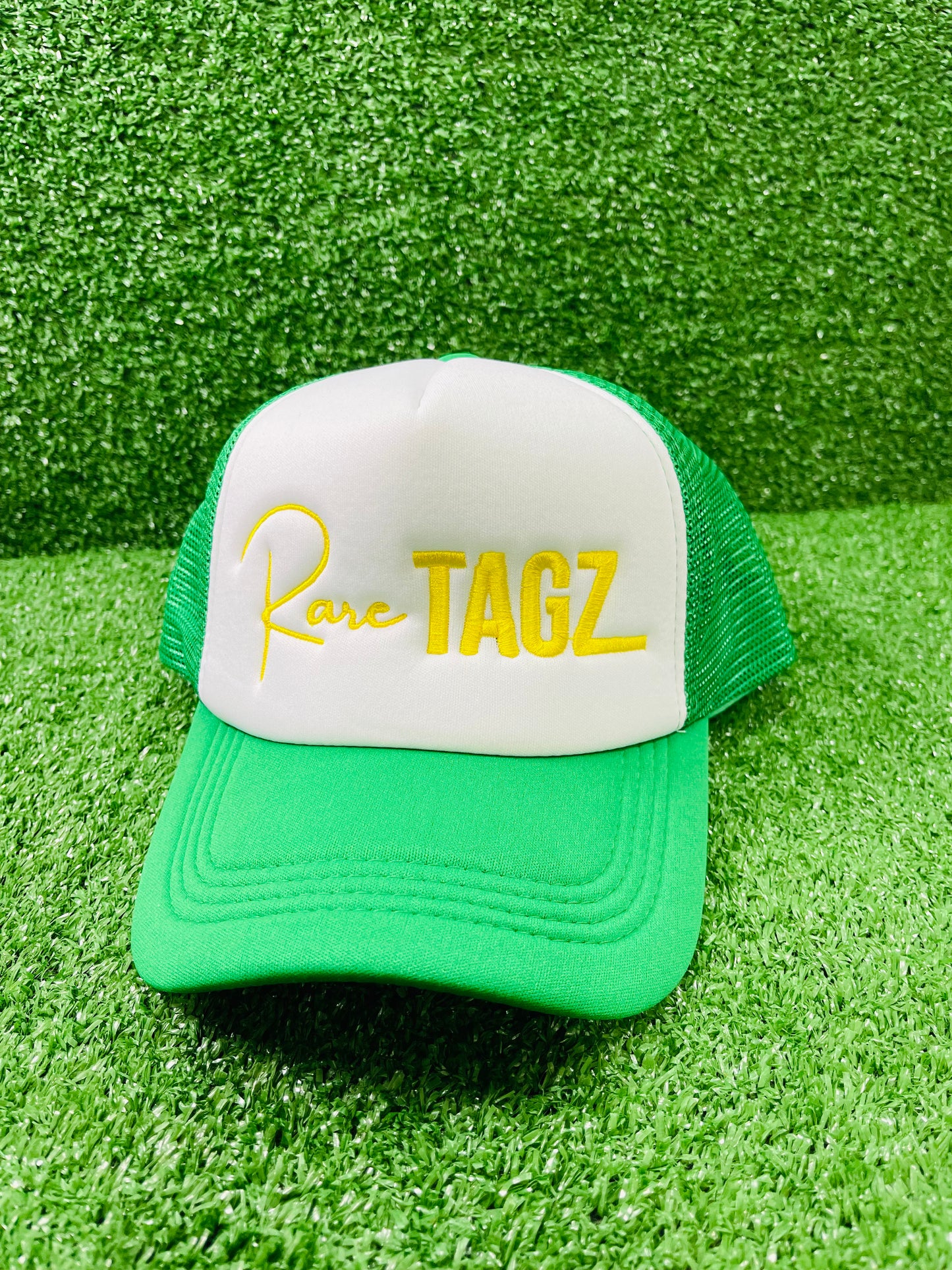 Front view of white and green trucker hat with Yellow "Rare Tagz" embroidery. Side angle of hat showing clean stitching and mesh back.