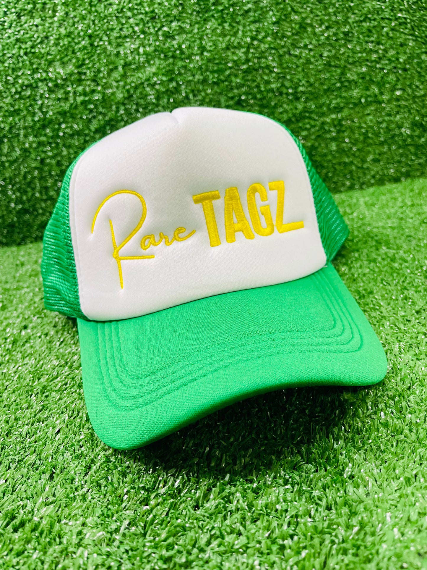 Front view of white and green trucker hat with Yellow "Rare Tagz" embroidery. Side angle of hat showing clean stitching and mesh back.