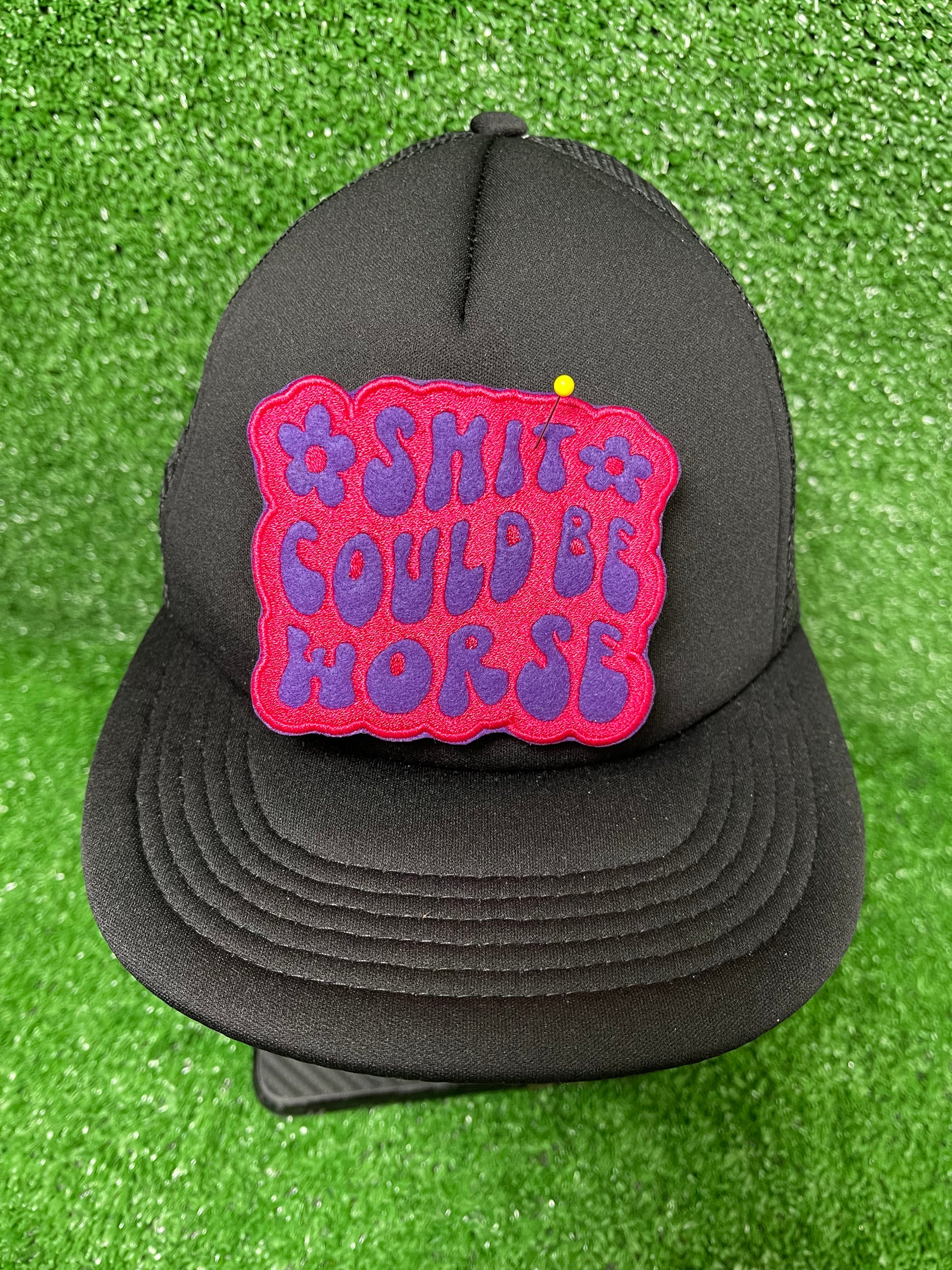 Embroidered patch with the phrase Shit Could be Worse in bold purple lettering on a pink background. The design is simple yet impactful, adding a touch of humor and resilience to any jacket, backpack or trucker hat.