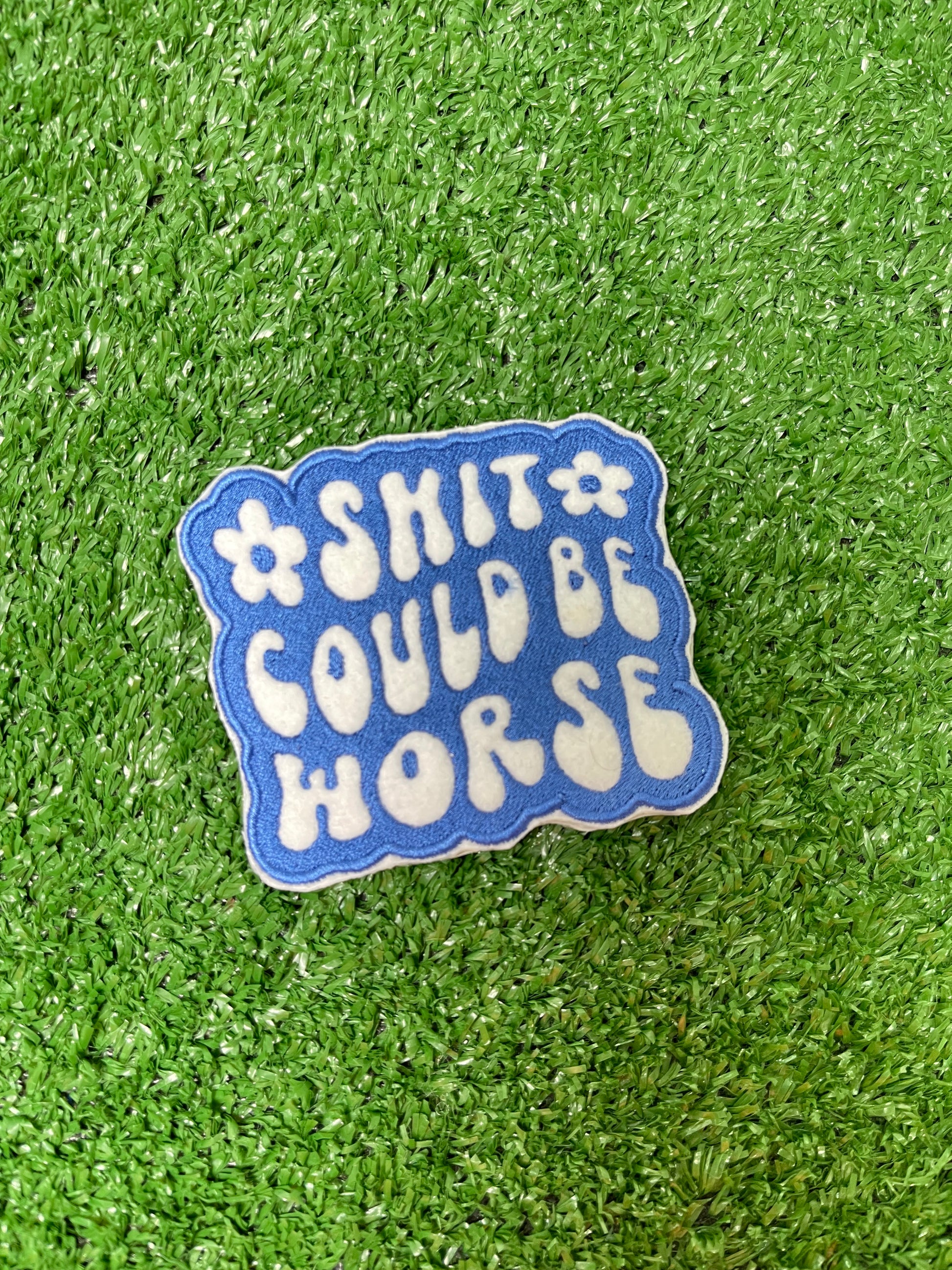 Embroidered patch with the phrase Shit Could be Worse in bold white lettering on a blue background. The design is simple yet impactful, adding a touch of humor and resilience to any jacket, backpack or trucker hat.