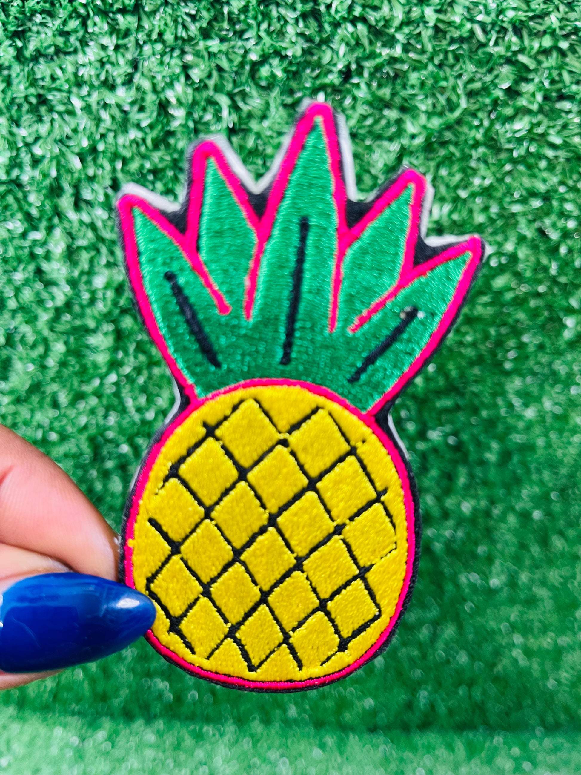 Pineapple-shaped patch held by a hand on a green textured background