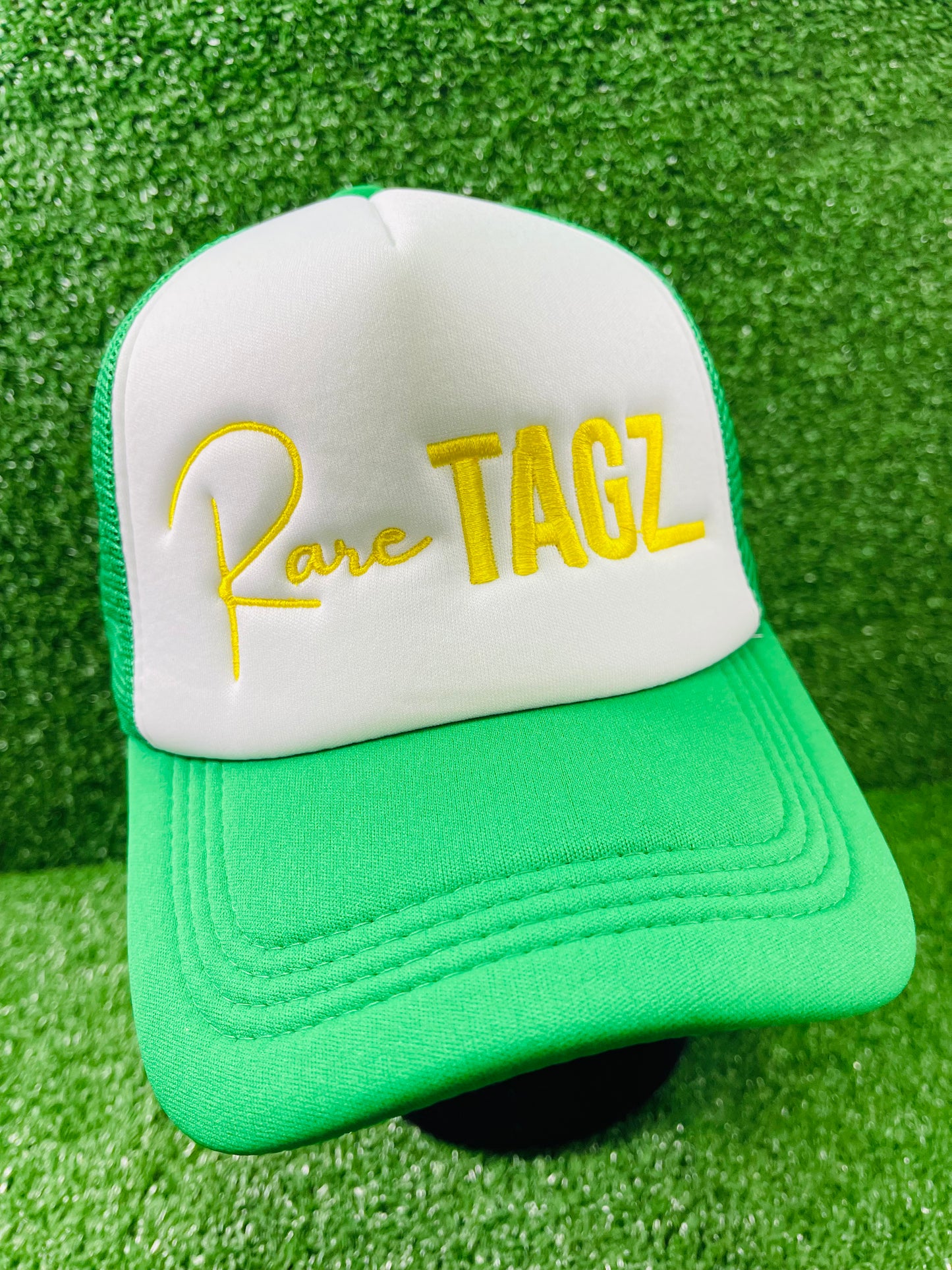 Front view of white and green trucker hat with Yellow "Rare Tagz" embroidery. Side angle of hat showing clean stitching and mesh back.
