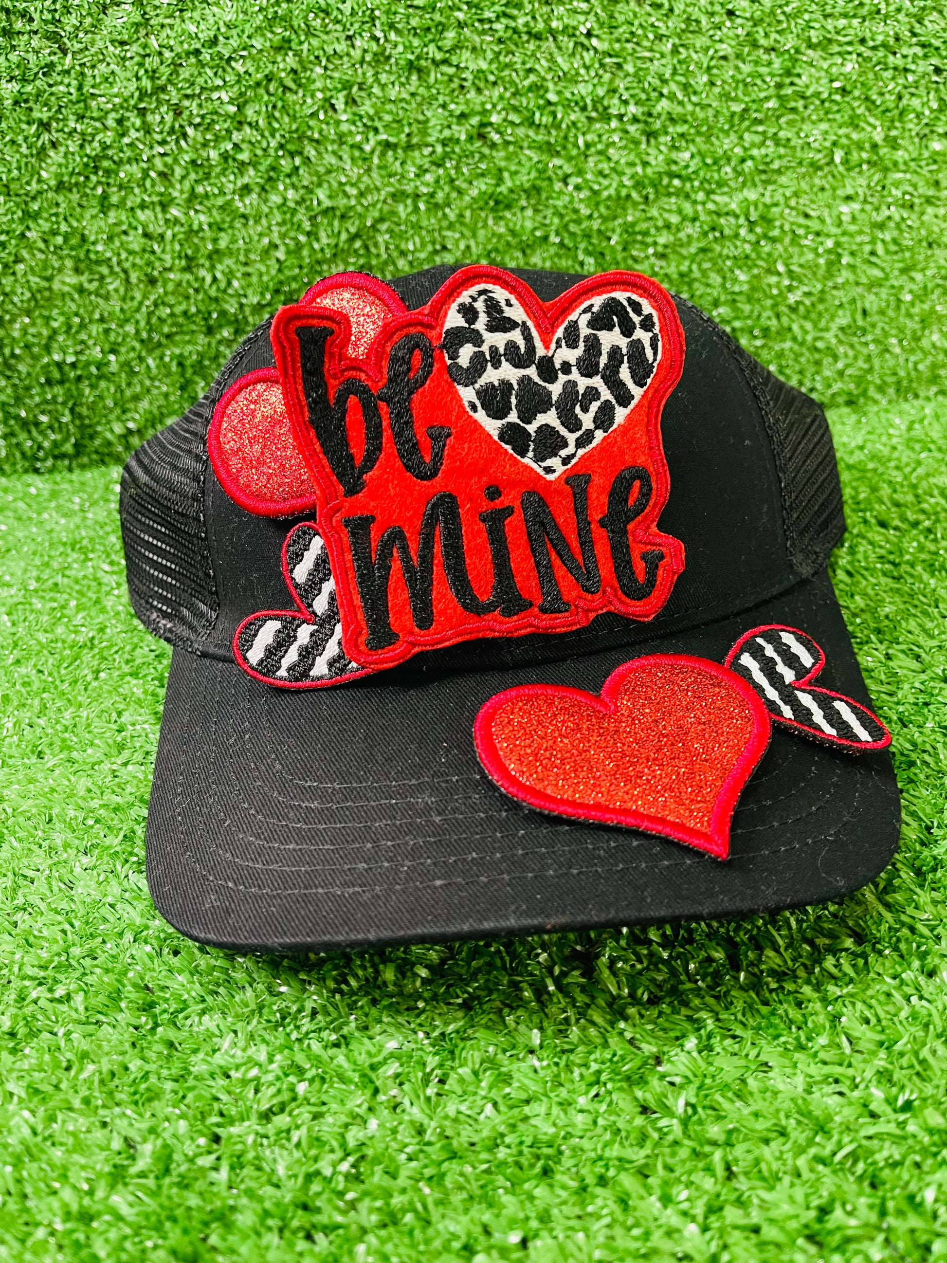 Valentine's Day patch set featuring a bold Be Mine design with a leopard heart, two red glitter hearts, and two black and white zebra stripped hearts displayed on a green grass background.