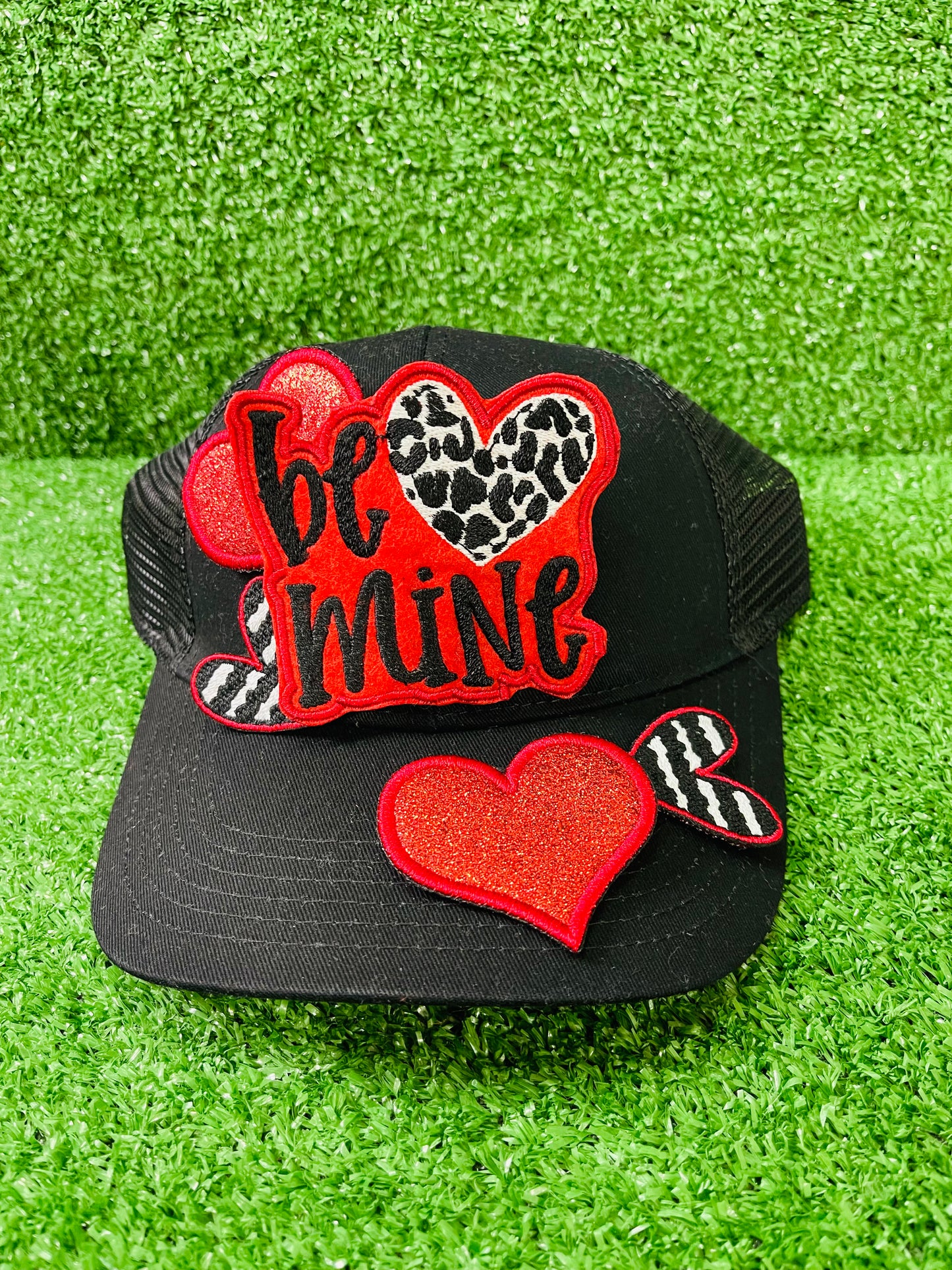 Valentine's Day patch set featuring a bold Be Mine design with a leopard heart, two red glitter hearts, and two black and white zebra stripped hearts displayed on a green grass background.