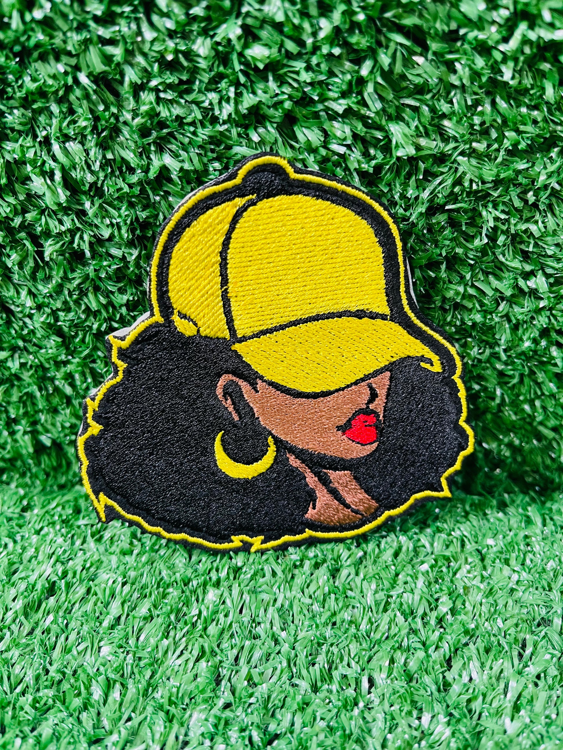 Embroidered patch of a woman wearing a yellow cap on green grass
