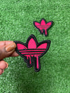 Detailed view of a pink Adidas iron-on patch with the classic trefoil logo and three stripes, perfect for adding a stylish, personalized touch to clothing.