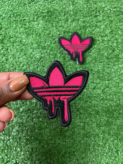 Detailed view of a pink Adidas iron-on patch with the classic trefoil logo and three stripes, perfect for adding a stylish, personalized touch to clothing.