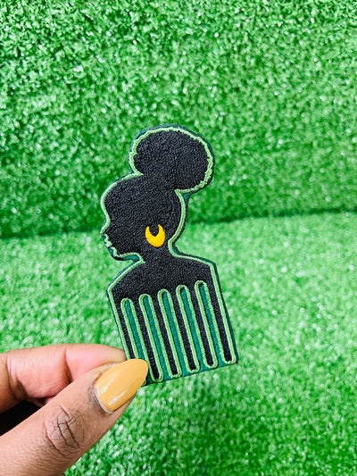 Silhouette of a woman with a natural bun, wearing a gold earring, incorporated into an afro pick design; green black embroidery with bold detailing.