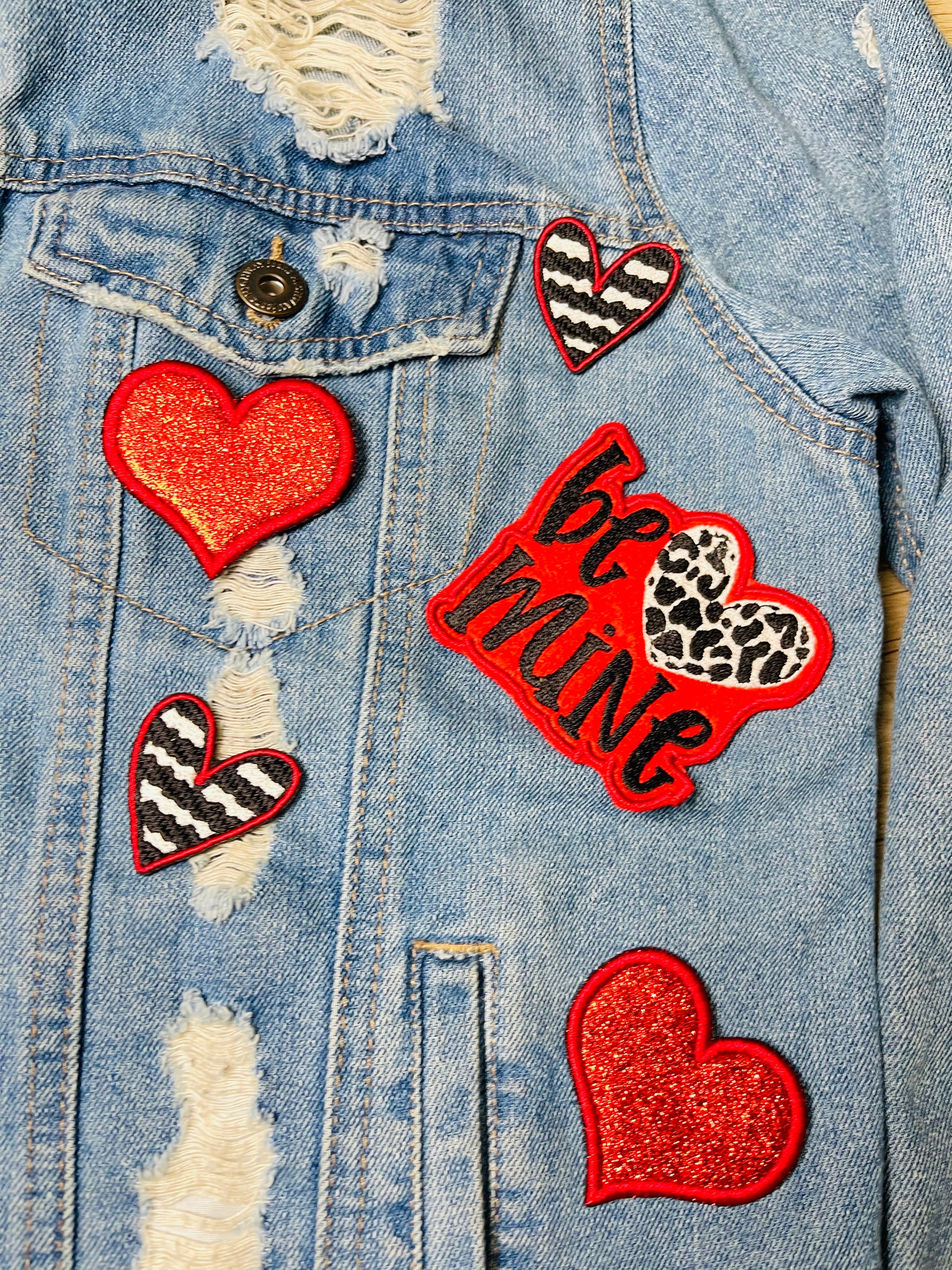 Valentine's Day patch set featuring a bold Be Mine design with a leopard heart, two red glitter hearts, and two black and white zebra stripped hearts displayed on a green grass background.