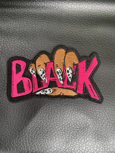 Embroidered iron-on patch featuring the word Black held by a hand with stylish-black and white nails. The letters Black are embroidered in bold pink stitching.