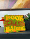 Bold and trendy iron-on patch featuring the phrase 'Book Club Baddie' in stylish lettering. Perfect for book lovers, this high-quality embroidered patch showcases vibrant colors and intricate stitching, ideal for adding a literary flair to jackets, backpacks, hats, and other clothing items.