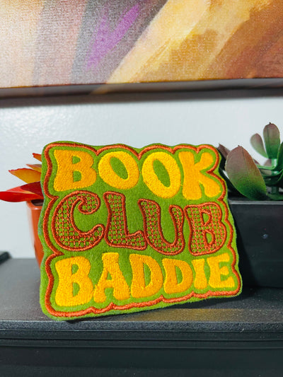 Bold and trendy iron-on patch featuring the phrase 'Book Club Baddie' in stylish lettering. Perfect for book lovers, this high-quality embroidered patch showcases vibrant colors and intricate stitching, ideal for adding a literary flair to jackets, backpacks, hats, and other clothing items.